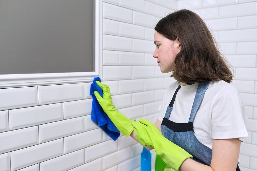 a woman in a white shirt and blue apron cleaning a white tile wall