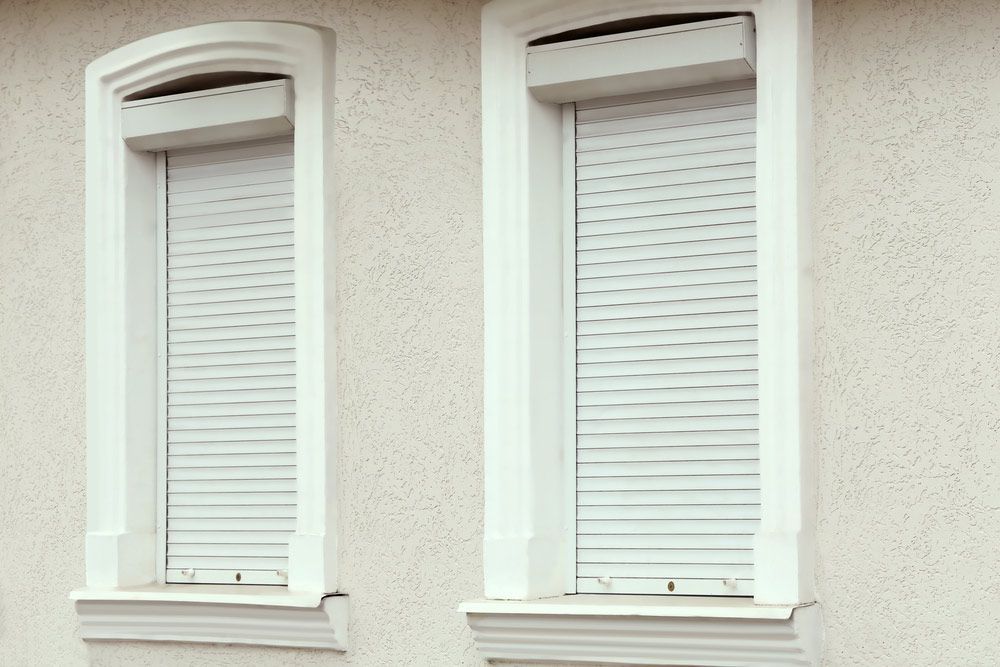 Two White Windows With Roller Shutters on the Side of a Building — Budget Screens & Awnings in Ballina, NSW