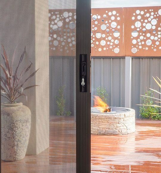 A Sliding Glass Door Leading to a Patio With a Fire Pit — Budget Screens & Awnings in South Lismore, NSW