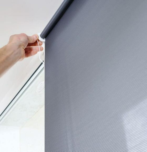 A Person is Adjusting a Roller Blind on a Window — Budget Screens & Awnings in South Lismore, NSW