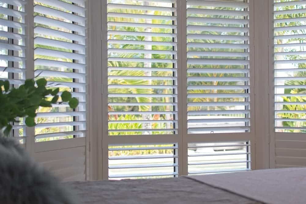 A Bedroom With a Bed and a Window With Shutters on It — Budget Screens & Awnings in South Lismore, NSW