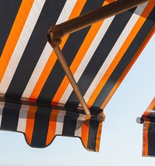 An Orange and Black Striped Awning Against a Blue Sky — Budget Screens & Awnings in South Lismore, NSW