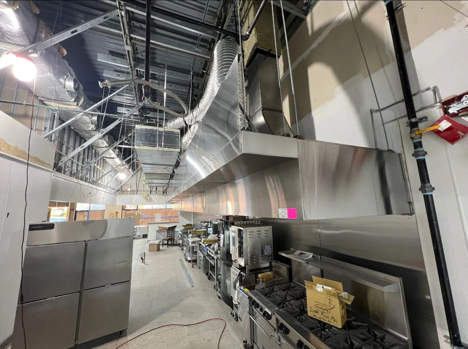Restaurant kitchen under construction, stainless steel hood, equipment, unfinished ceiling.