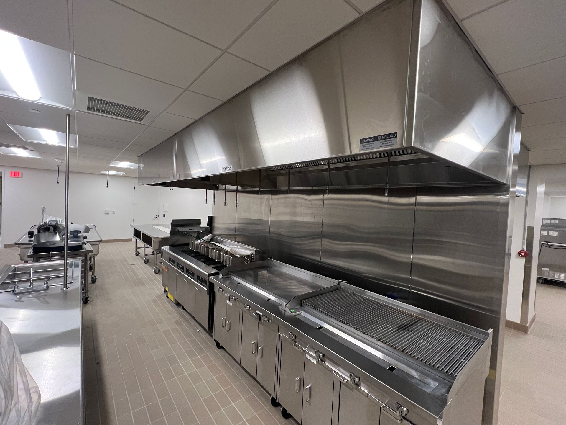 A clean, commercial kitchen with stainless steel appliances, a large exhaust hood, and a tiled floor.