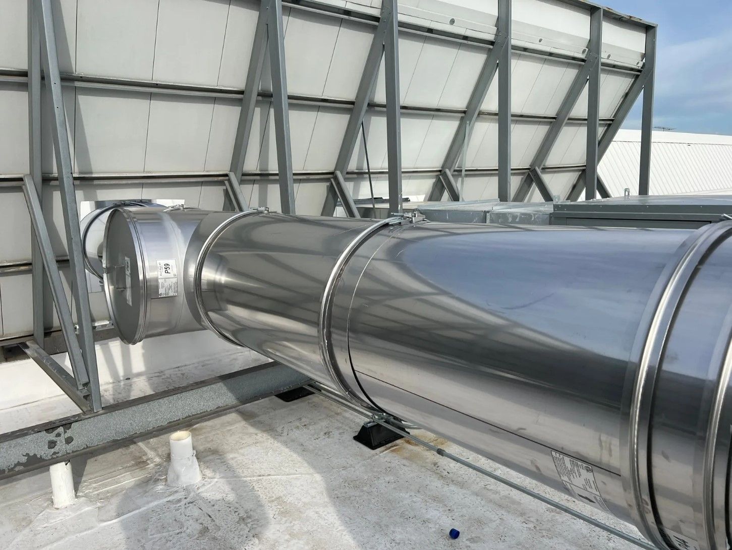 Shiny metal ductwork on a rooftop with white panels and gray structural supports.