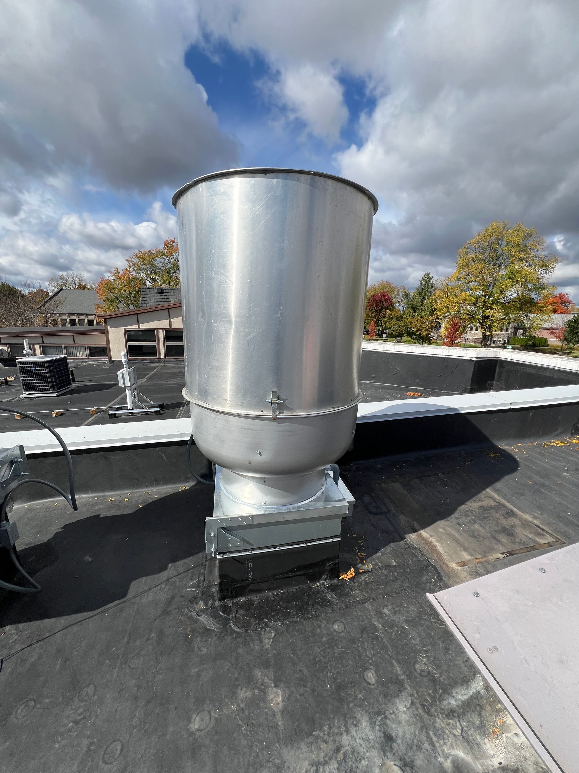 Large cylindrical metal vent on a flat roof under a partly cloudy sky.