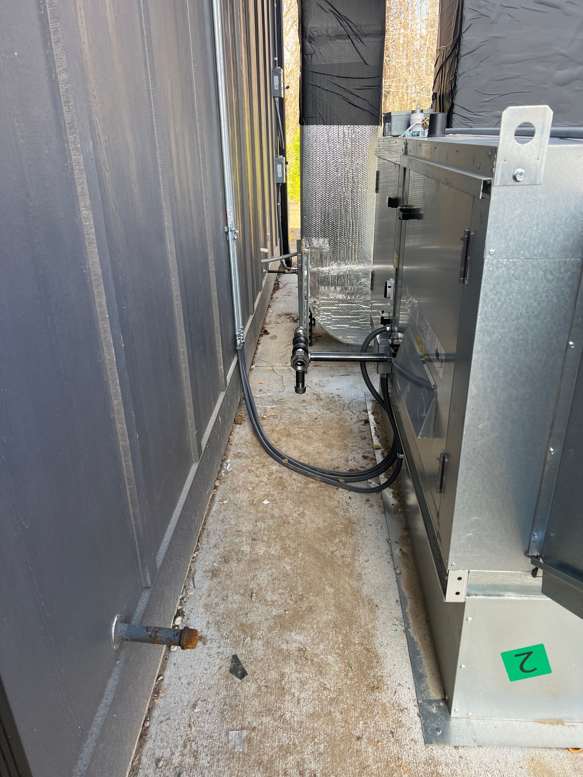 Narrow outdoor pathway between gray walls and HVAC equipment.