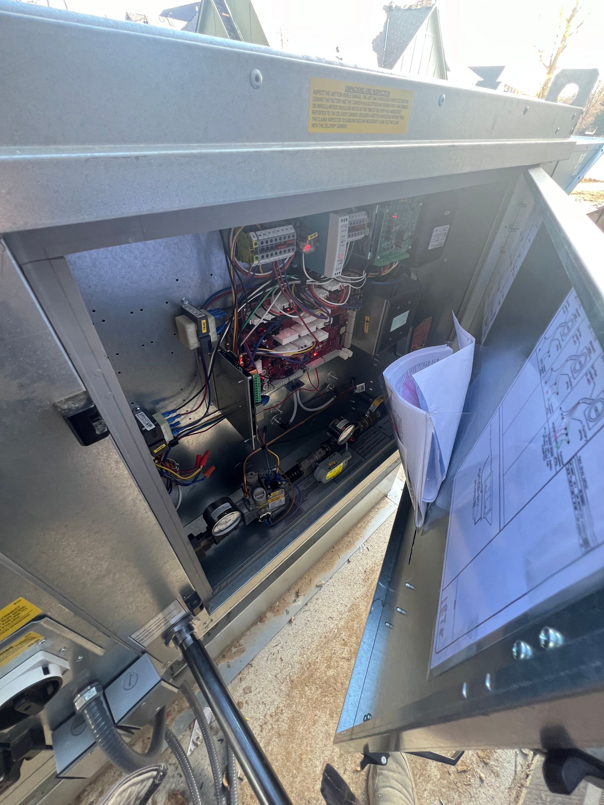 Open electrical cabinet with wires, circuits, and a schematic sheet. Gray metal, complex internal components.
