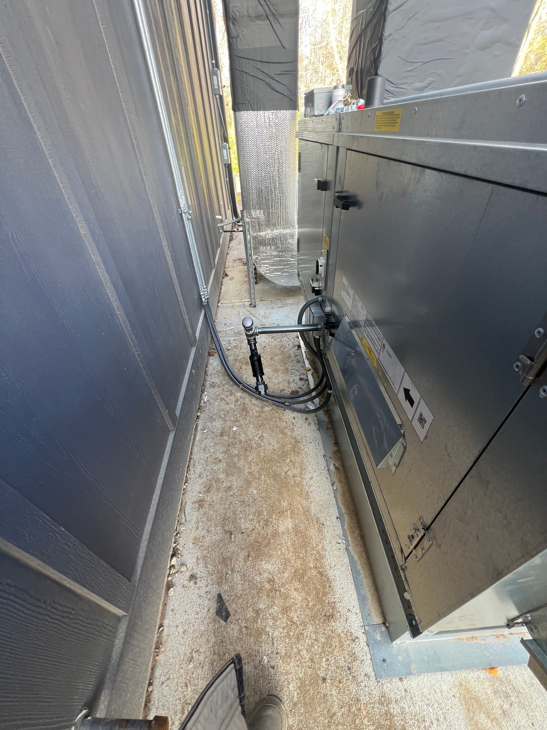 A narrow outdoor space between metal structures with a chain and electrical cables.