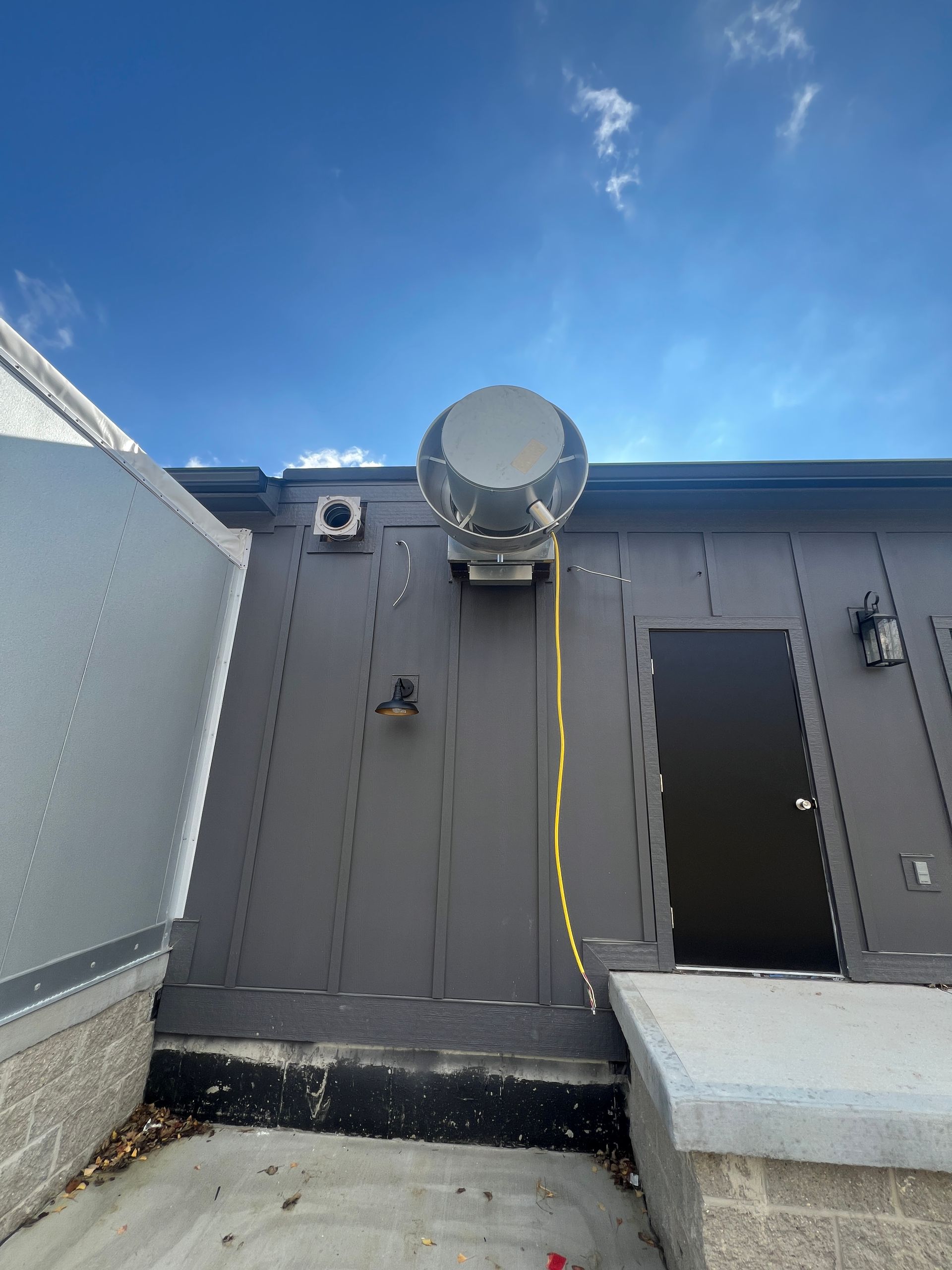 A large ventilation unit mounted on the side of a building under a blue sky.