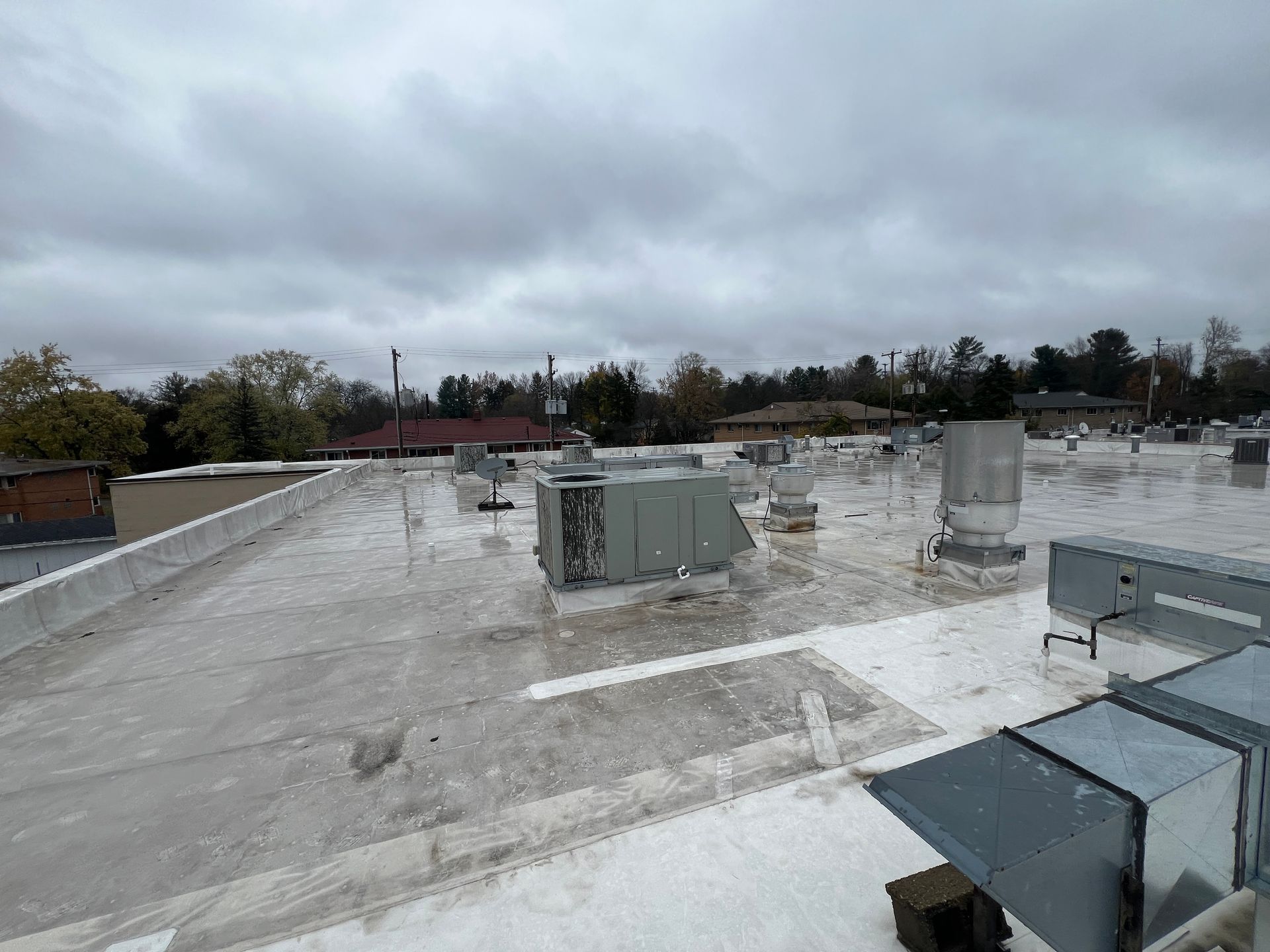 Flat commercial rooftop with various HVAC units under a cloudy sky.