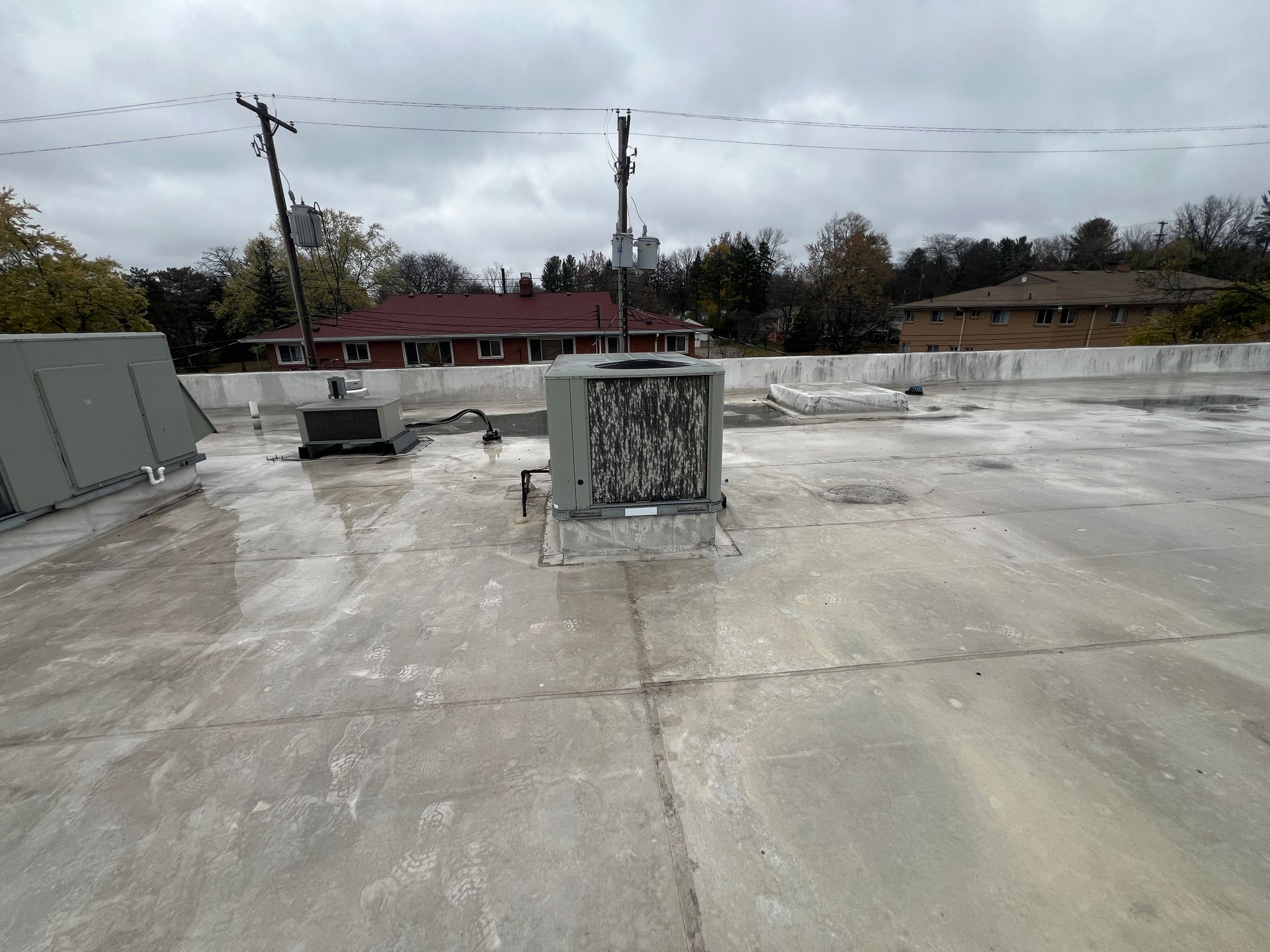 Flat rooftop with HVAC unit, power lines, and distant buildings under overcast sky.