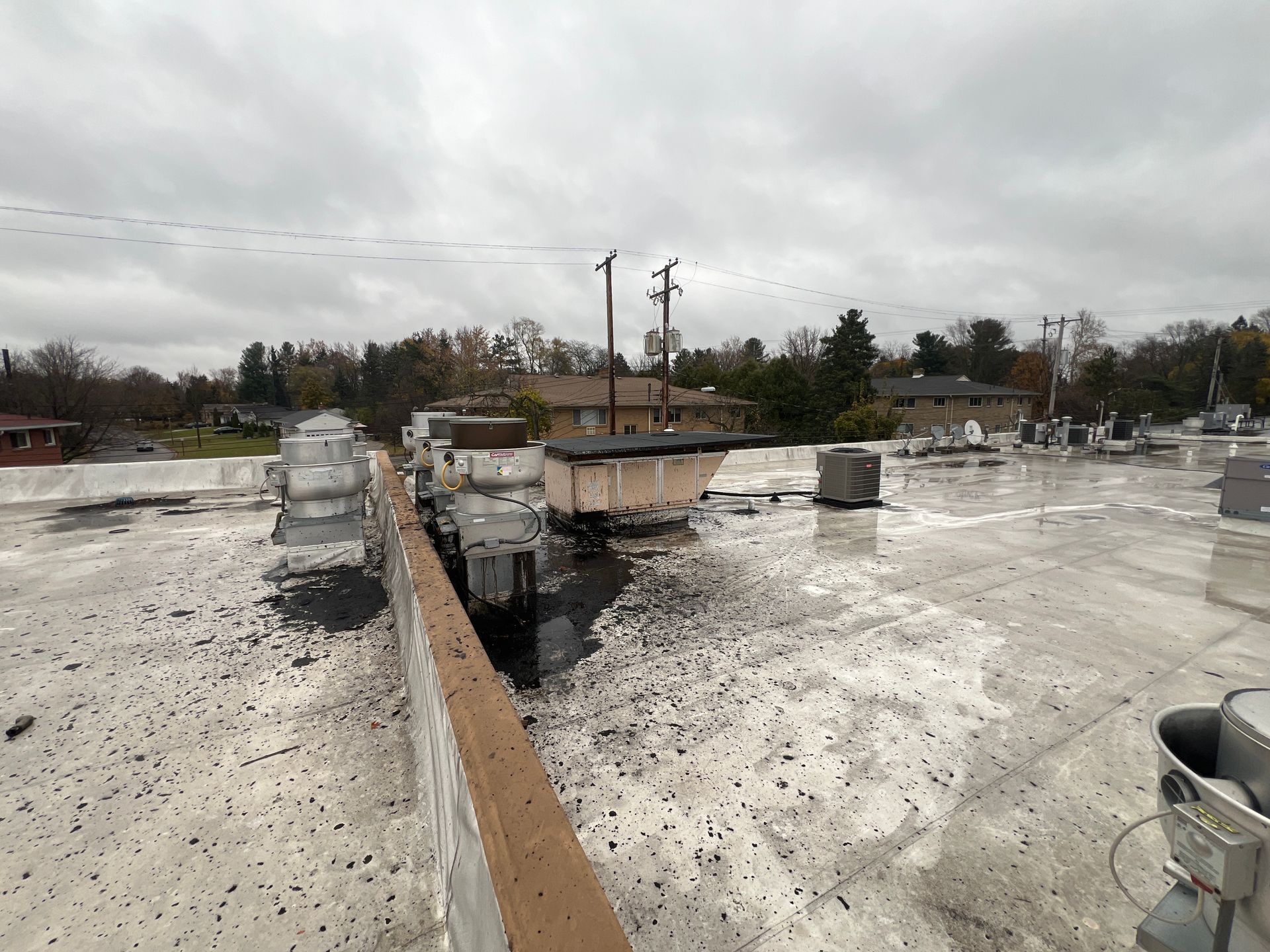 Commercial building roof with HVAC units, vents, and utility poles under a cloudy sky.