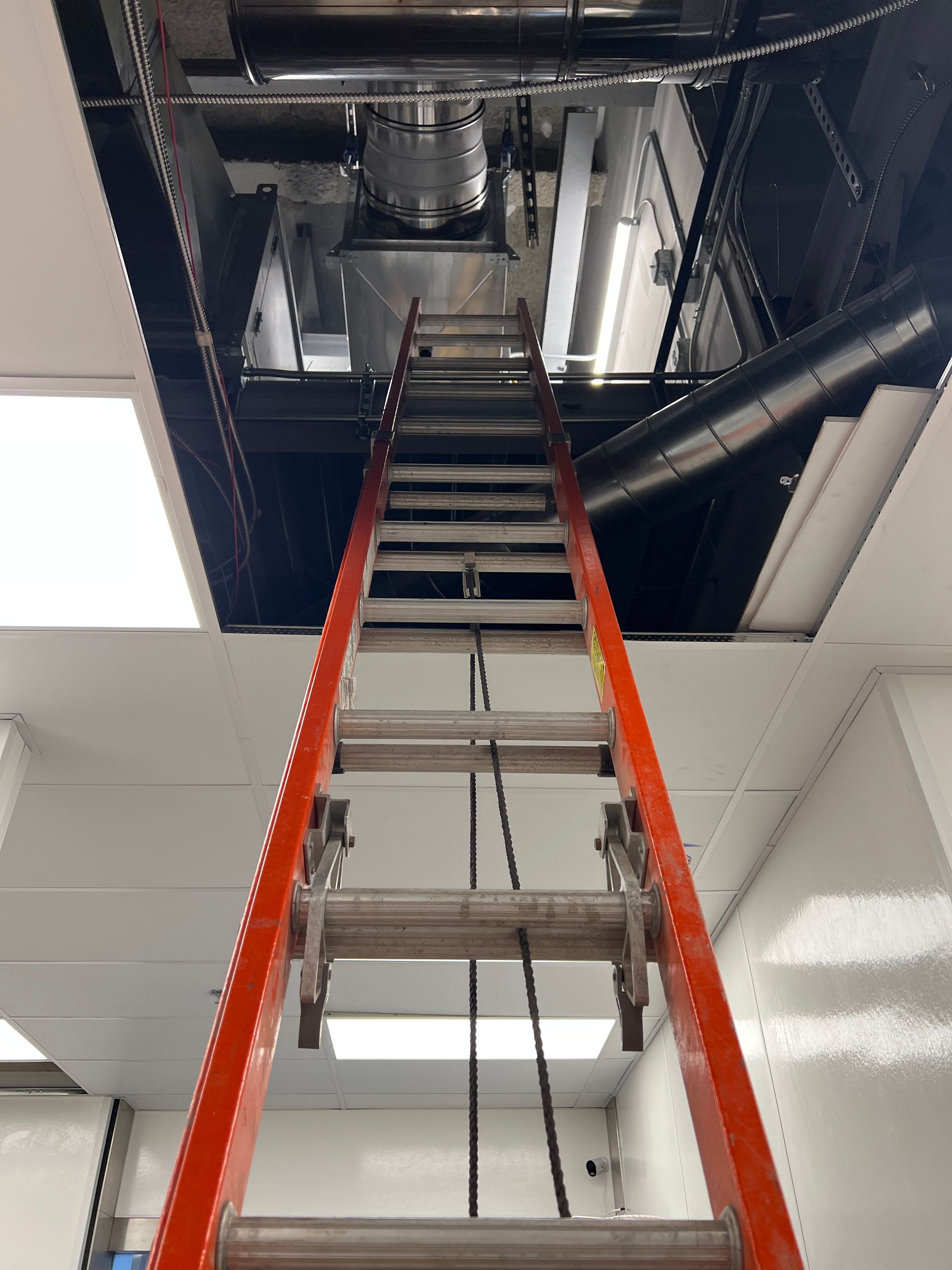 An orange ladder extending up through an opening in the ceiling, leading to equipment and machinery.