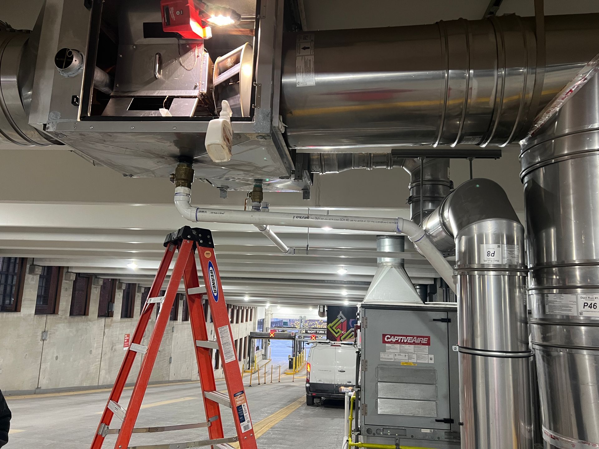 HVAC system being worked on in a building. A ladder is set up near pipes and ducts.