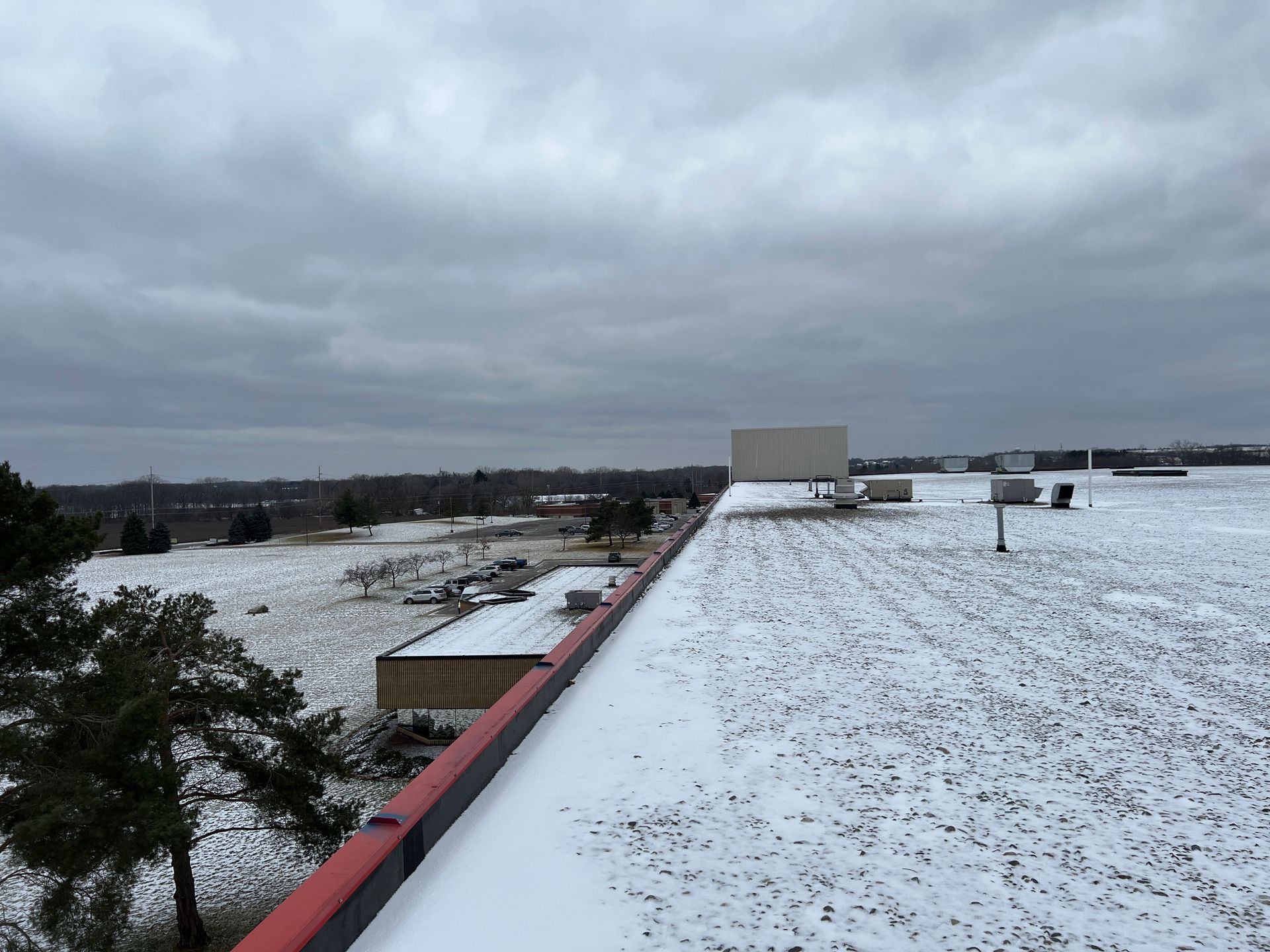 Snowy rooftop with view of field and cloudy sky.