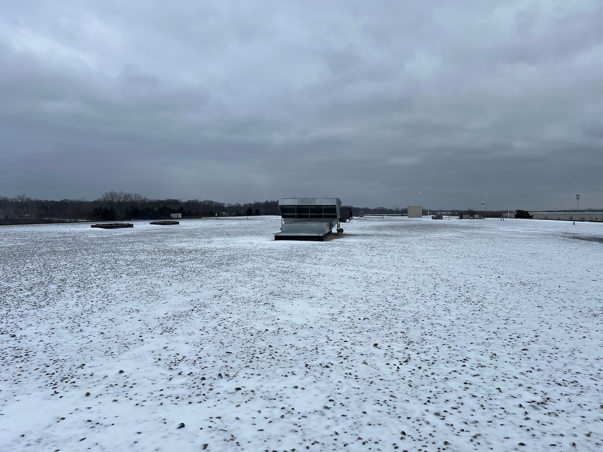 Rooftop covered in snow, with a cloudy sky above. Several mechanical units are visible.