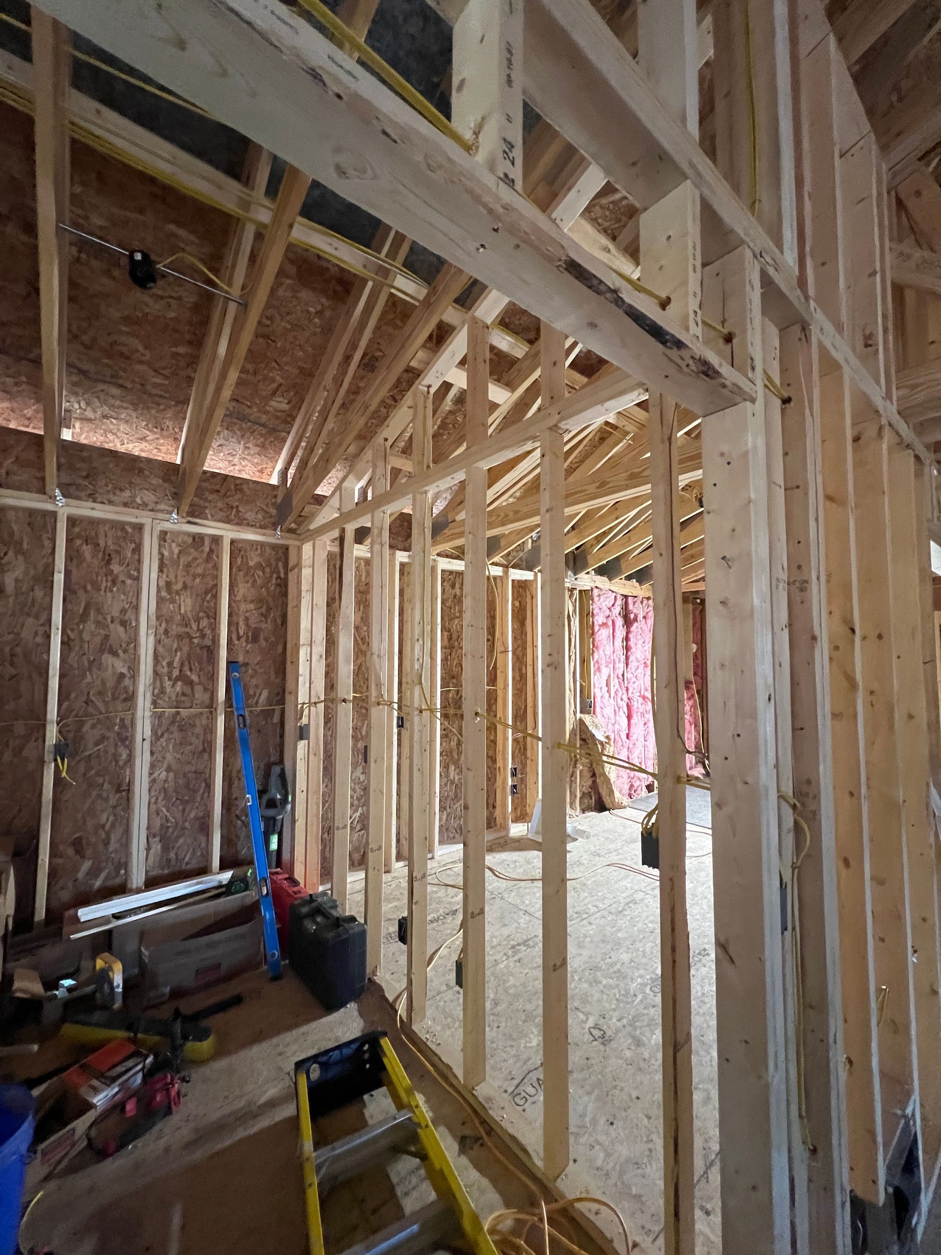 Interior view of a building under construction, showing wooden framing for walls, ceiling, and roof; tools and materials scattered.