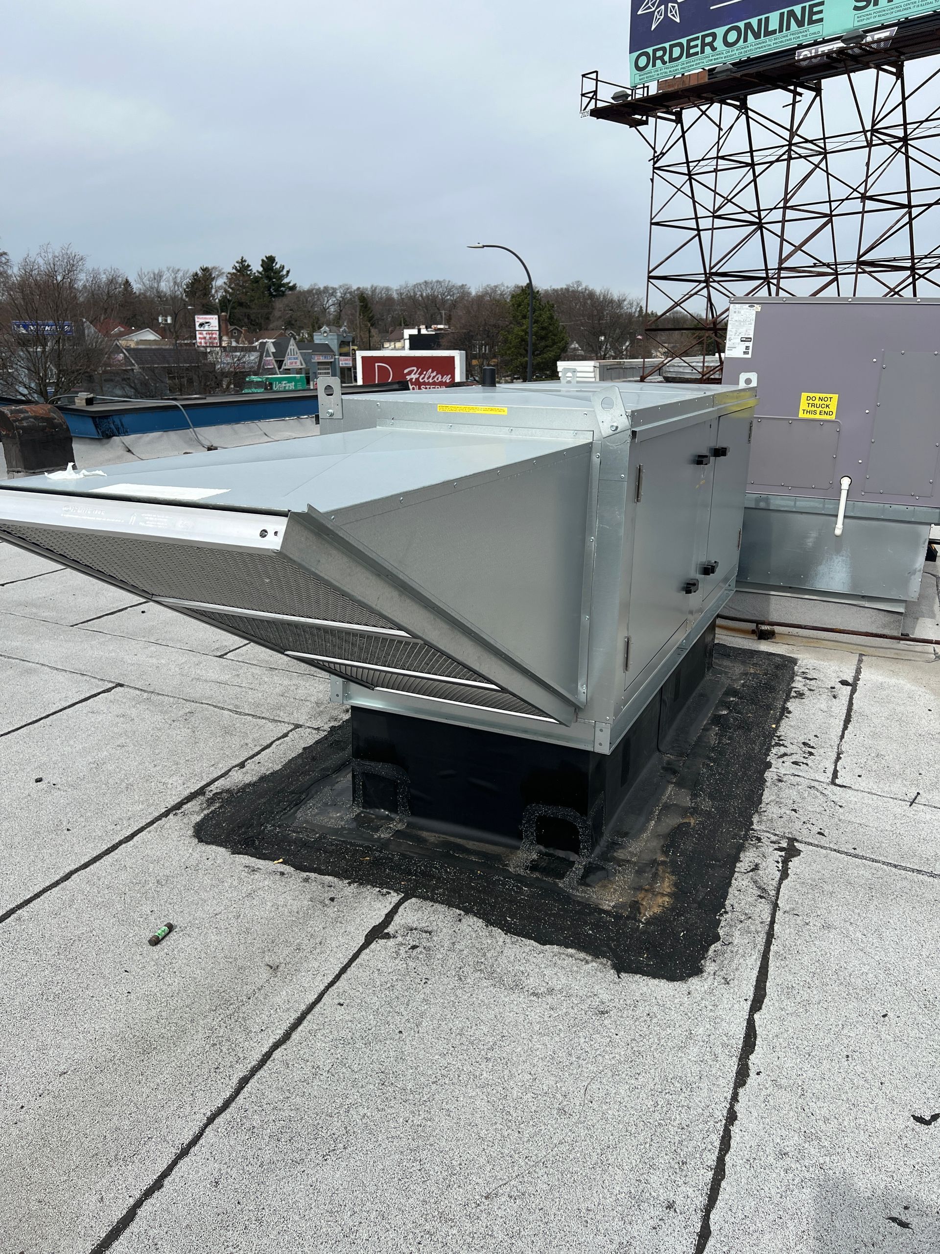 HVAC unit on a rooftop, angled metal with a mesh opening, mounted on a black base.