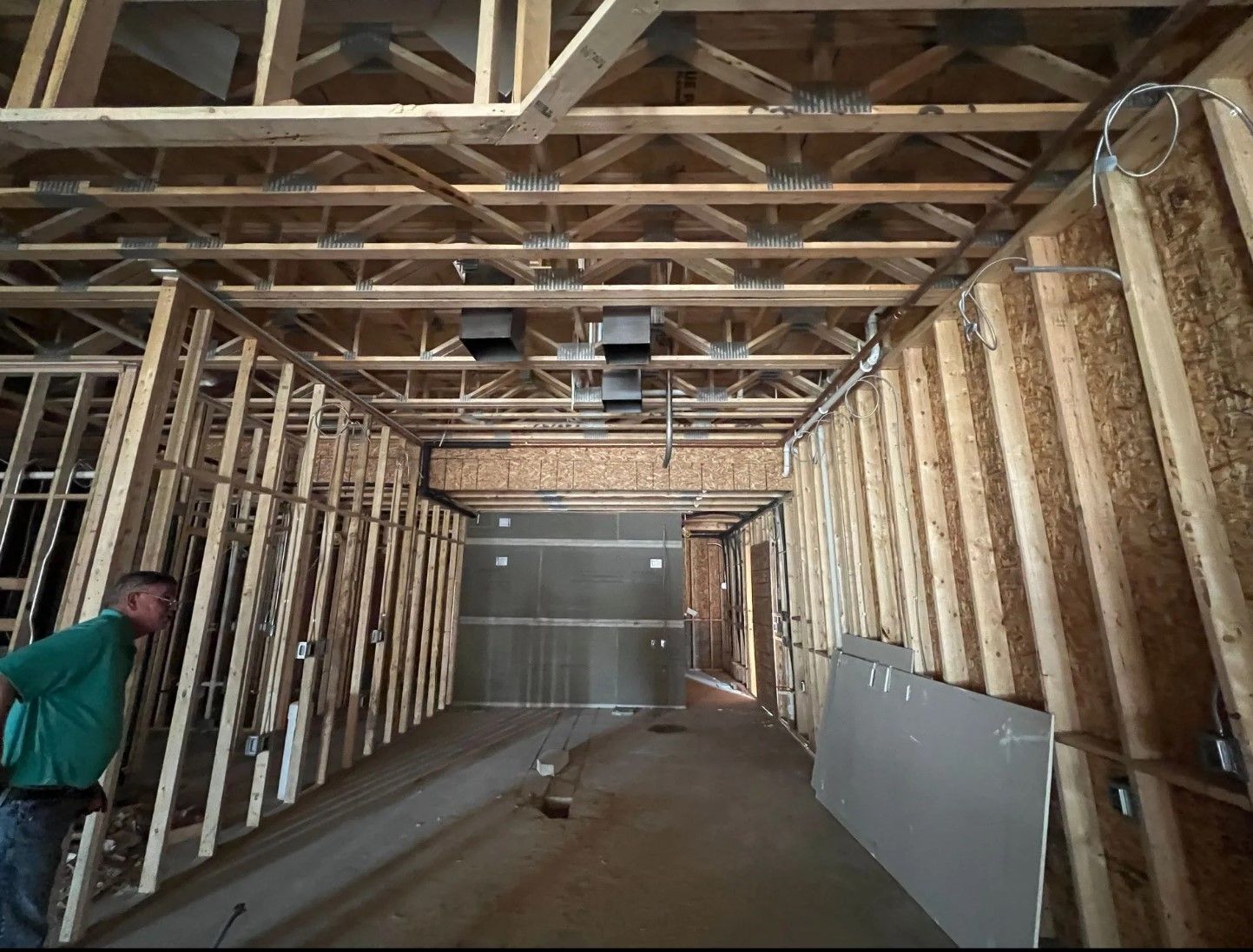 Construction site interior: wooden framework, man observing, exposed ceiling structure, unfinished walls.