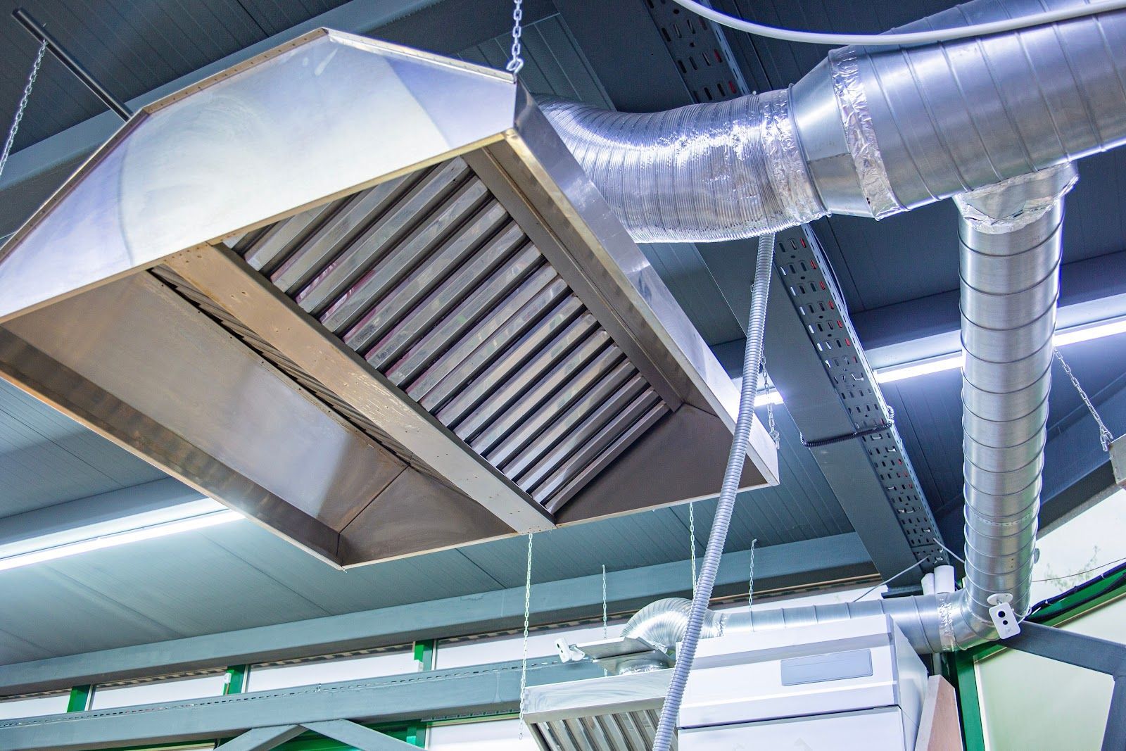 Commercial kitchen exhaust hood with ductwork, stainless steel, attached to ceiling.
