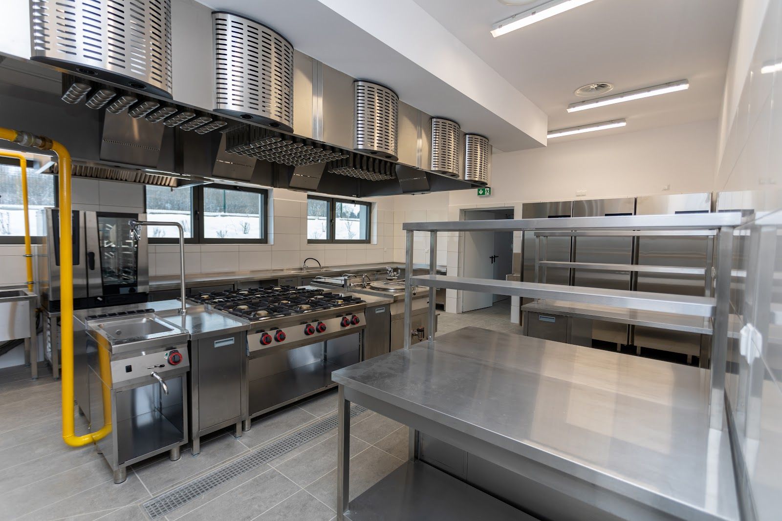 Commercial kitchen with stainless steel appliances and ventilation hoods.