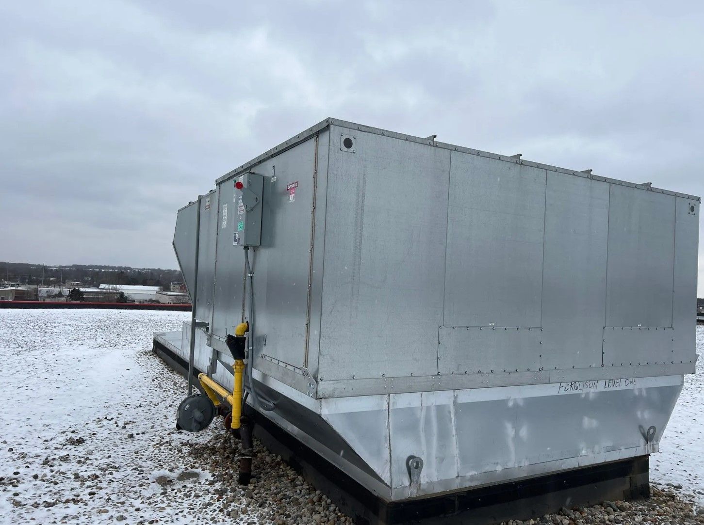 Large metallic HVAC unit on a snowy rooftop under an overcast sky.