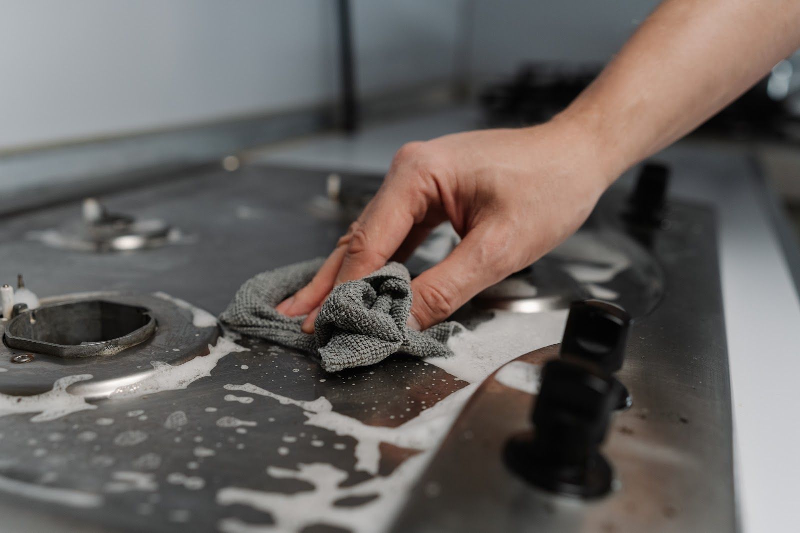 Hand wiping down a stainless steel stovetop with soapy sponge.