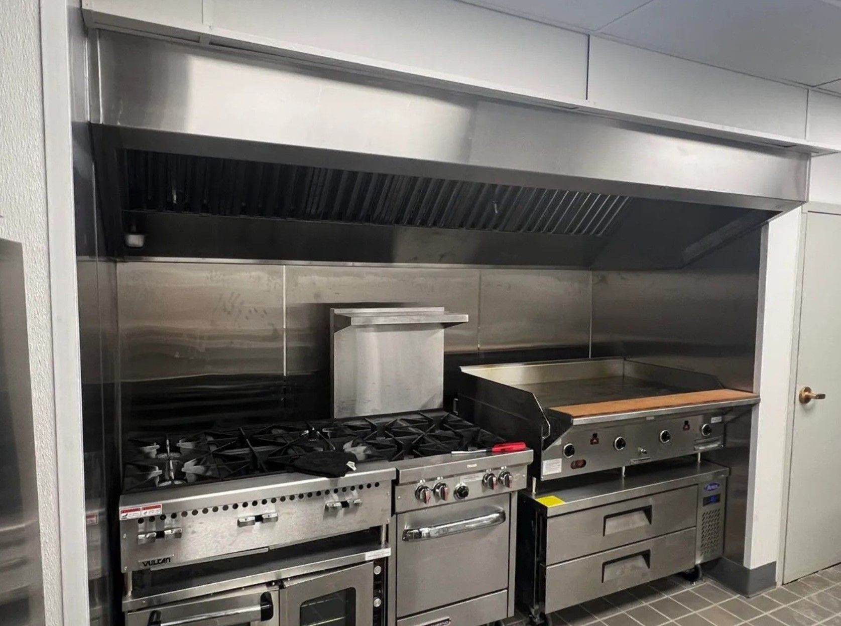 Commercial kitchen with stainless steel hood over gas range and griddle.