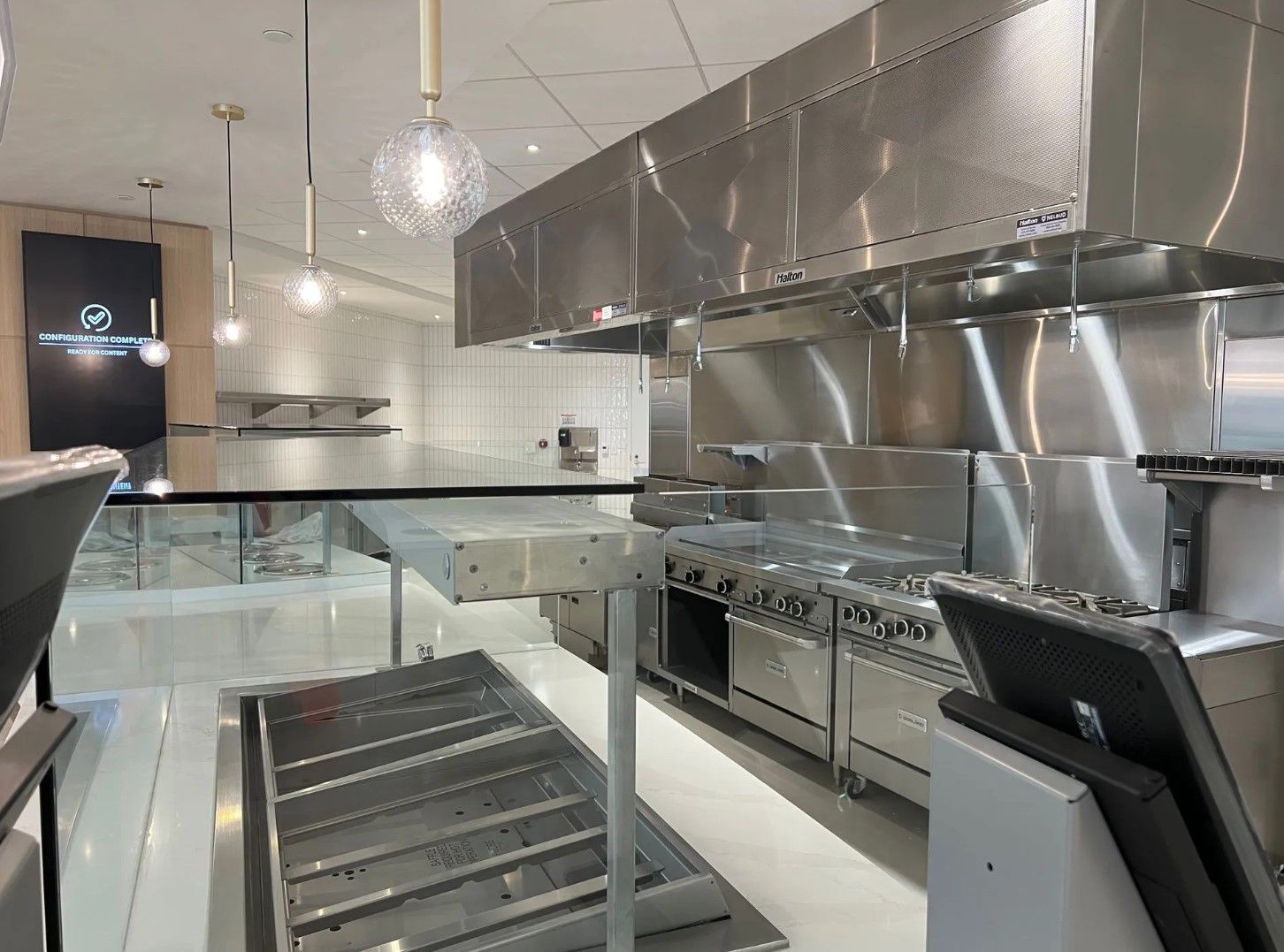 Stainless steel commercial kitchen with appliances and overhead vent.