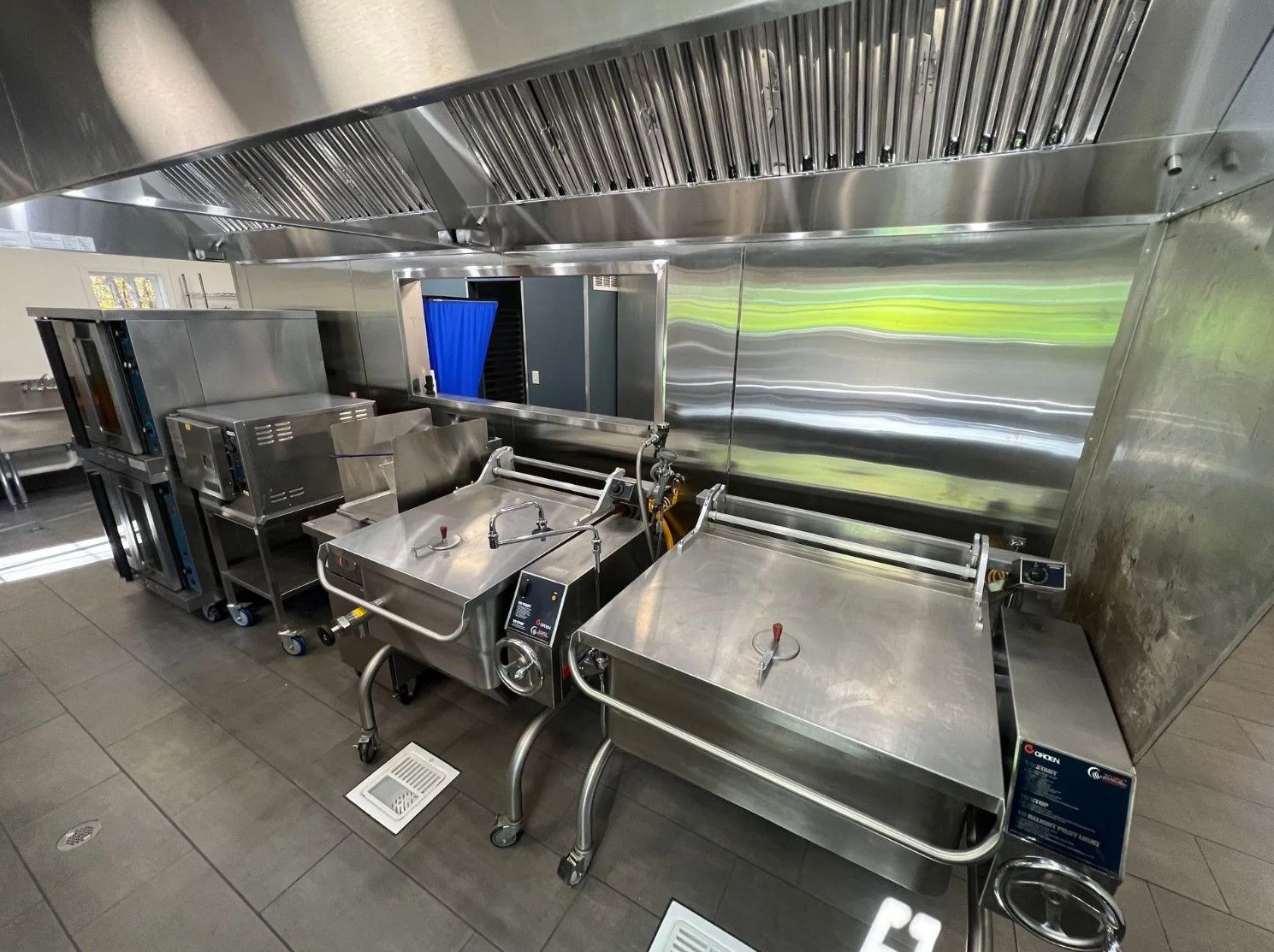 Commercial kitchen with stainless steel cooking equipment, ventilation hood.