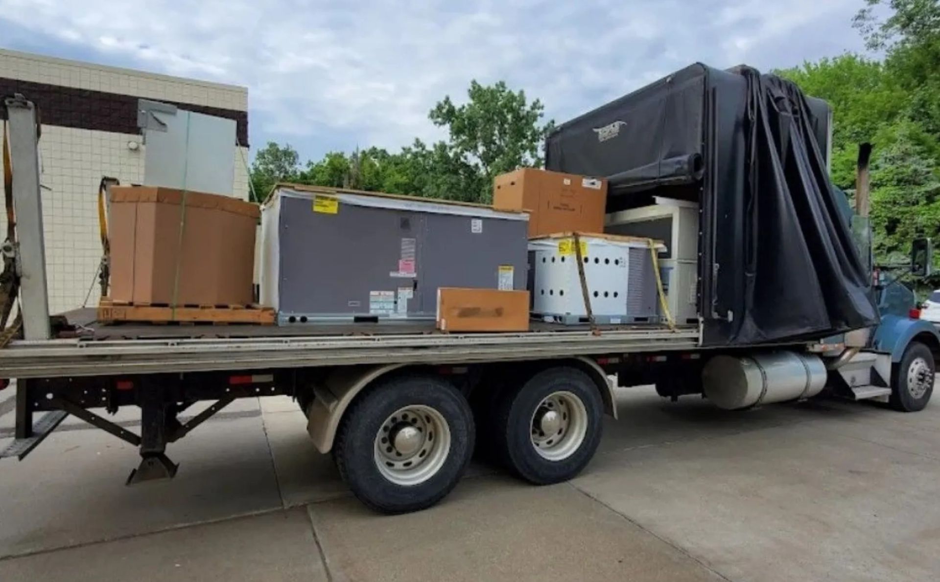 Semi-truck with a flatbed loaded with large boxes and equipment in an outdoor setting.