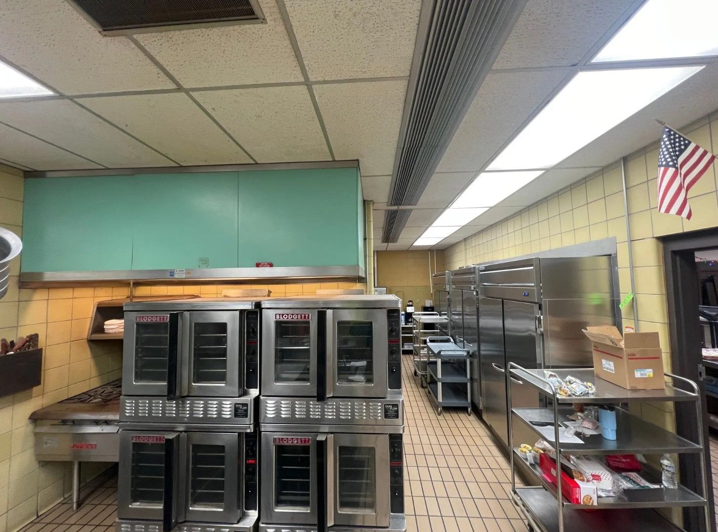 Commercial kitchen with ovens, stainless steel shelving, and a hanging American flag.