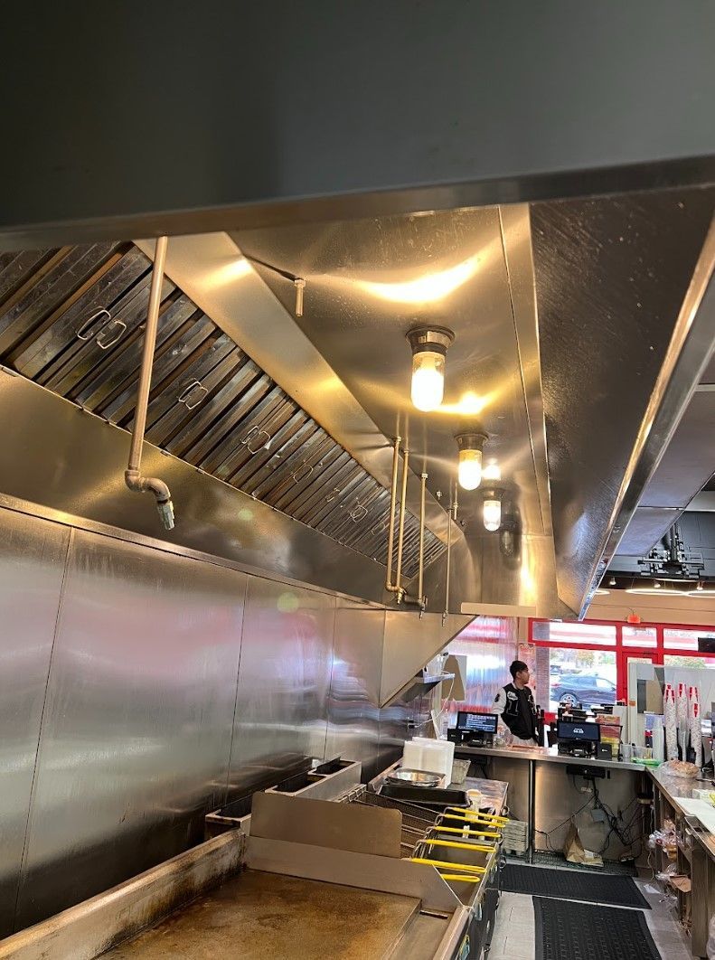 Stainless steel commercial kitchen range hood with lights over a cooking area.