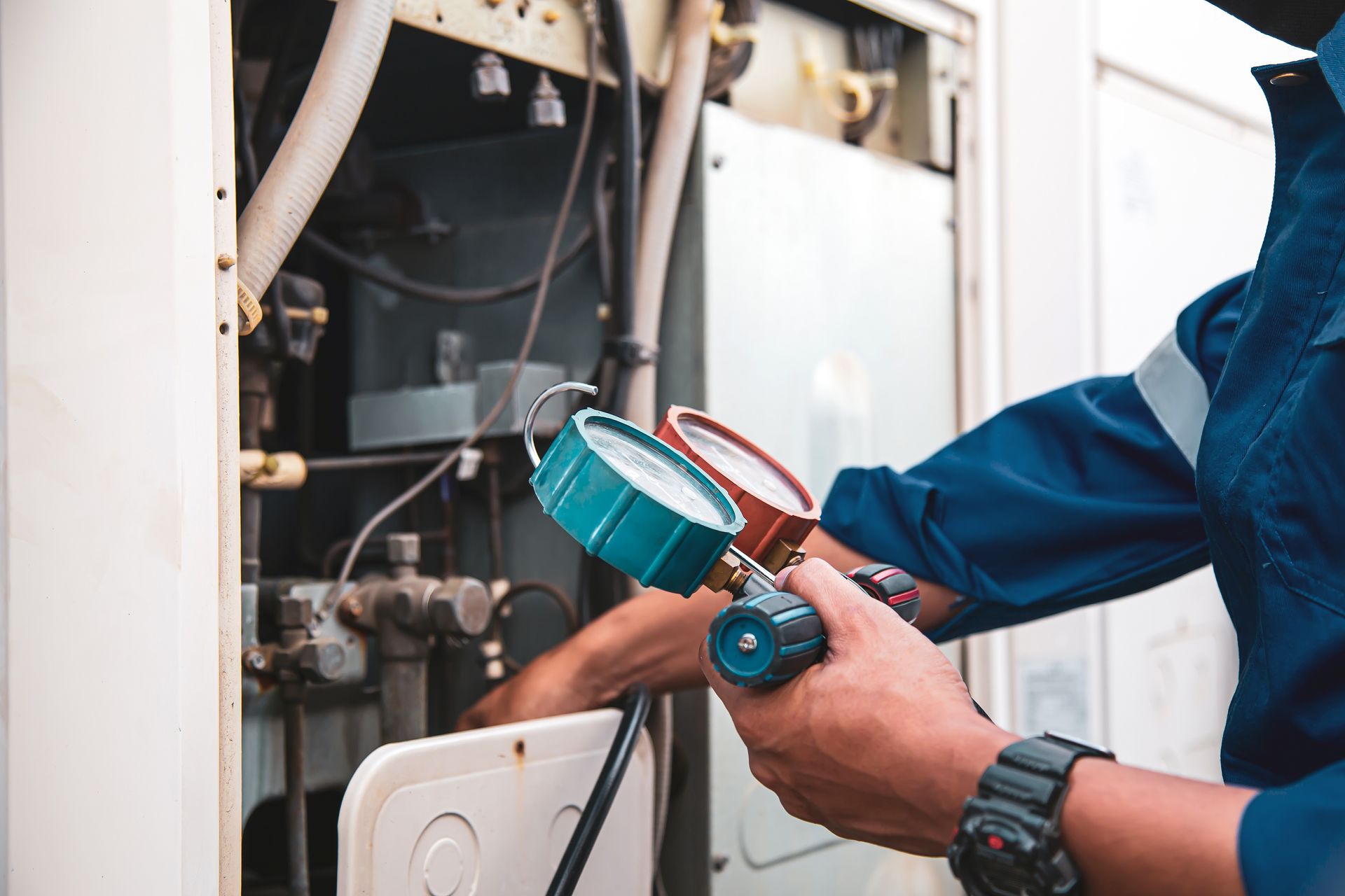 HVAC technician using gauges to inspect an air conditioning unit; close-up. Blue and white colors.