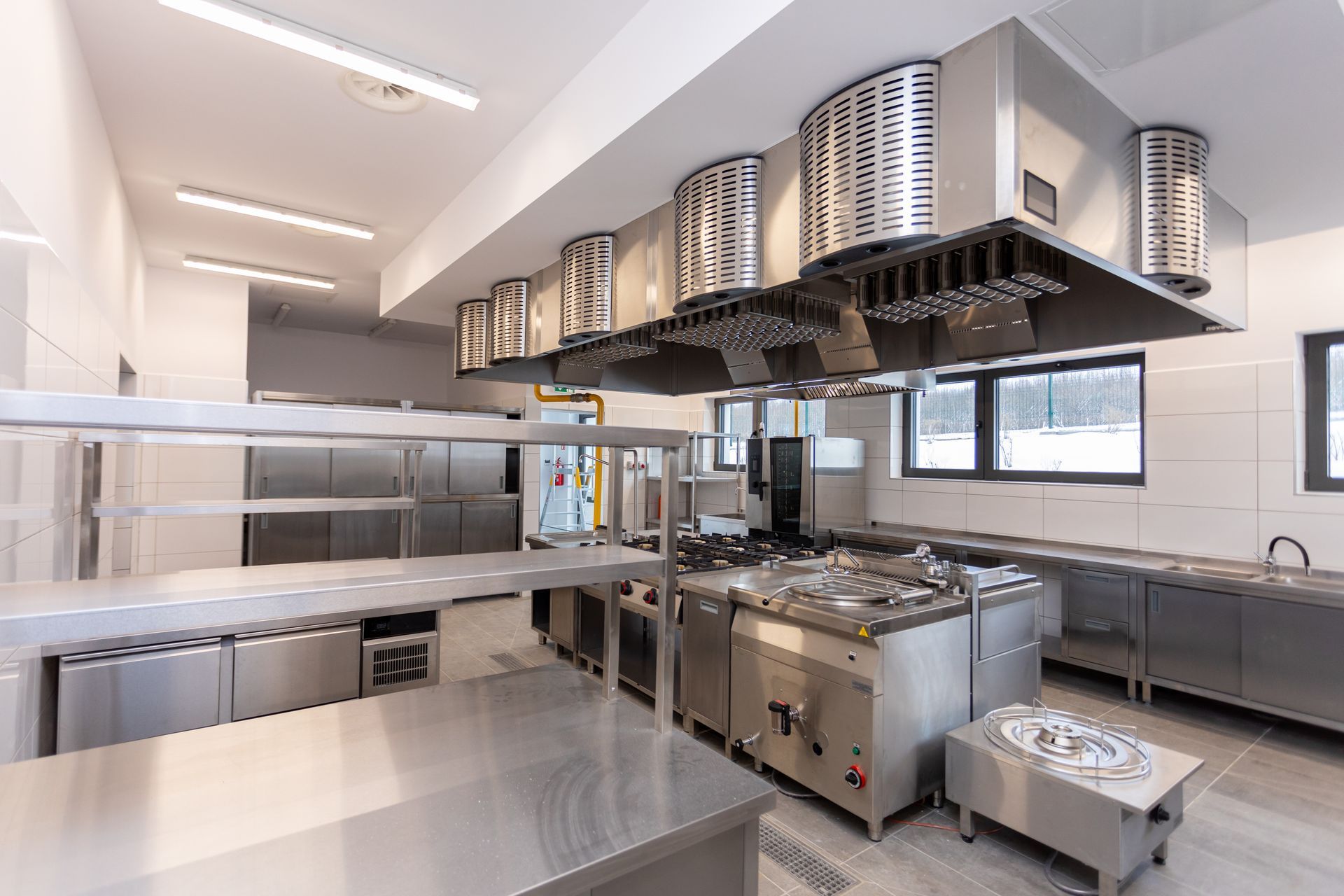A commercial kitchen with stainless steel appliances, ventilation hoods, and workspace.