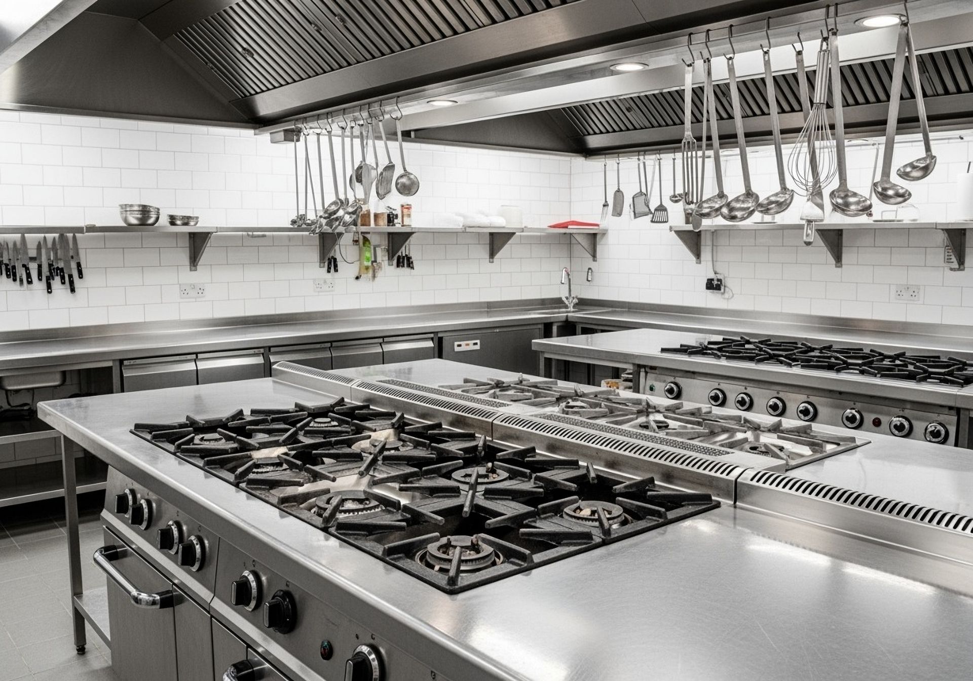 Commercial kitchen with stainless steel appliances, stovetops, and hanging utensils.