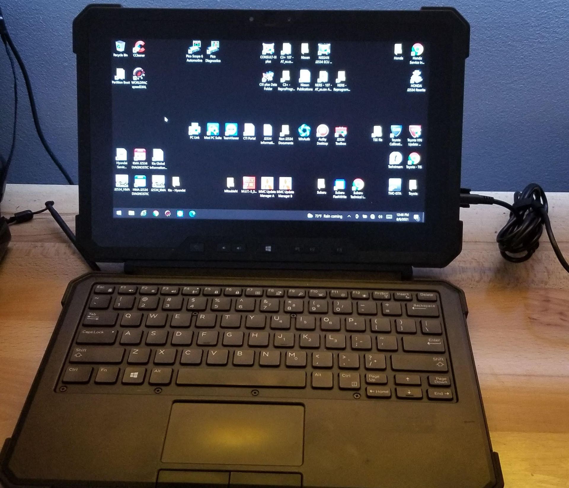 Rugged laptop with keyboard and screen displaying numerous icons, plugged in.