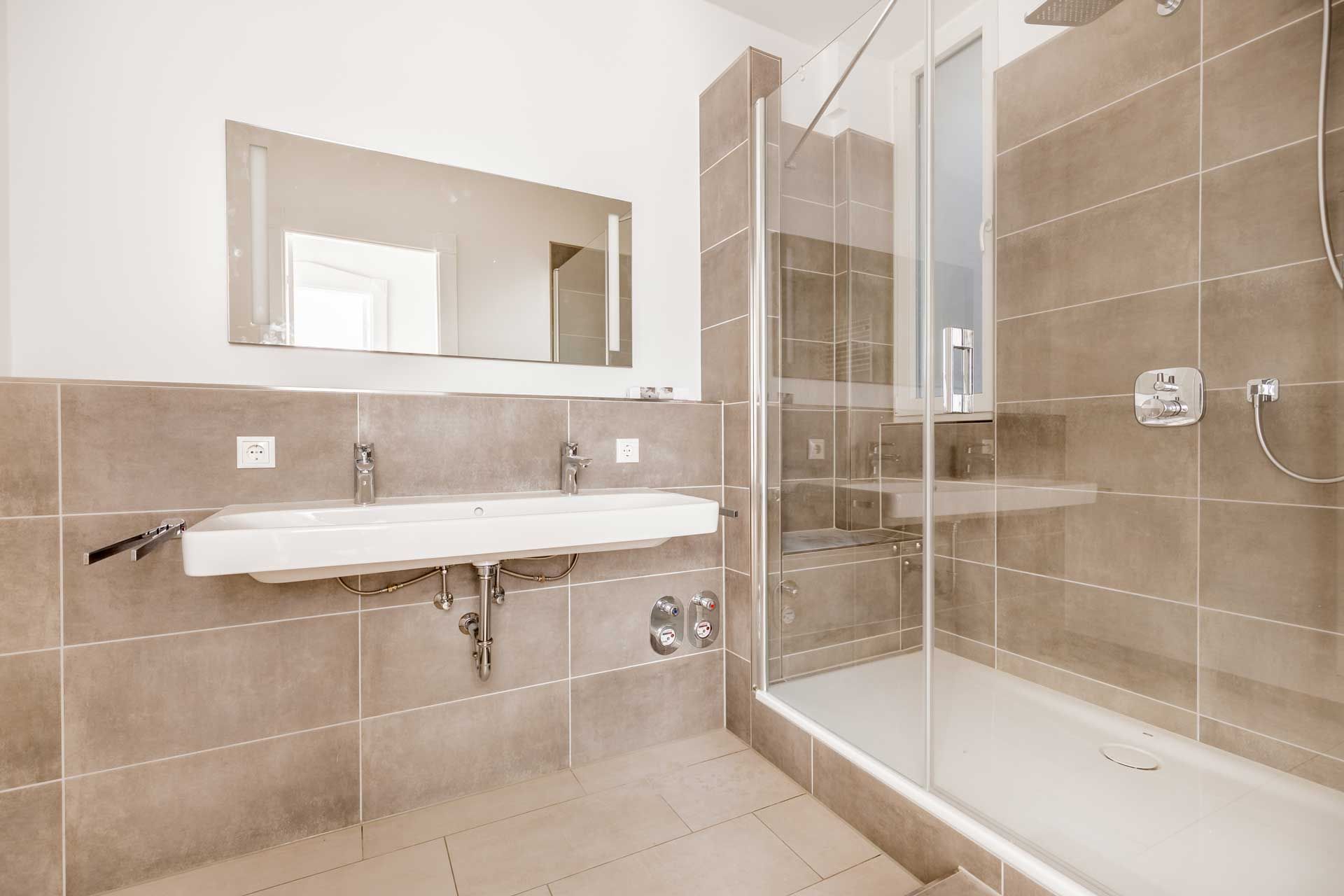 Modern bathroom with a glass shower, double sink, and neutral-colored tile.