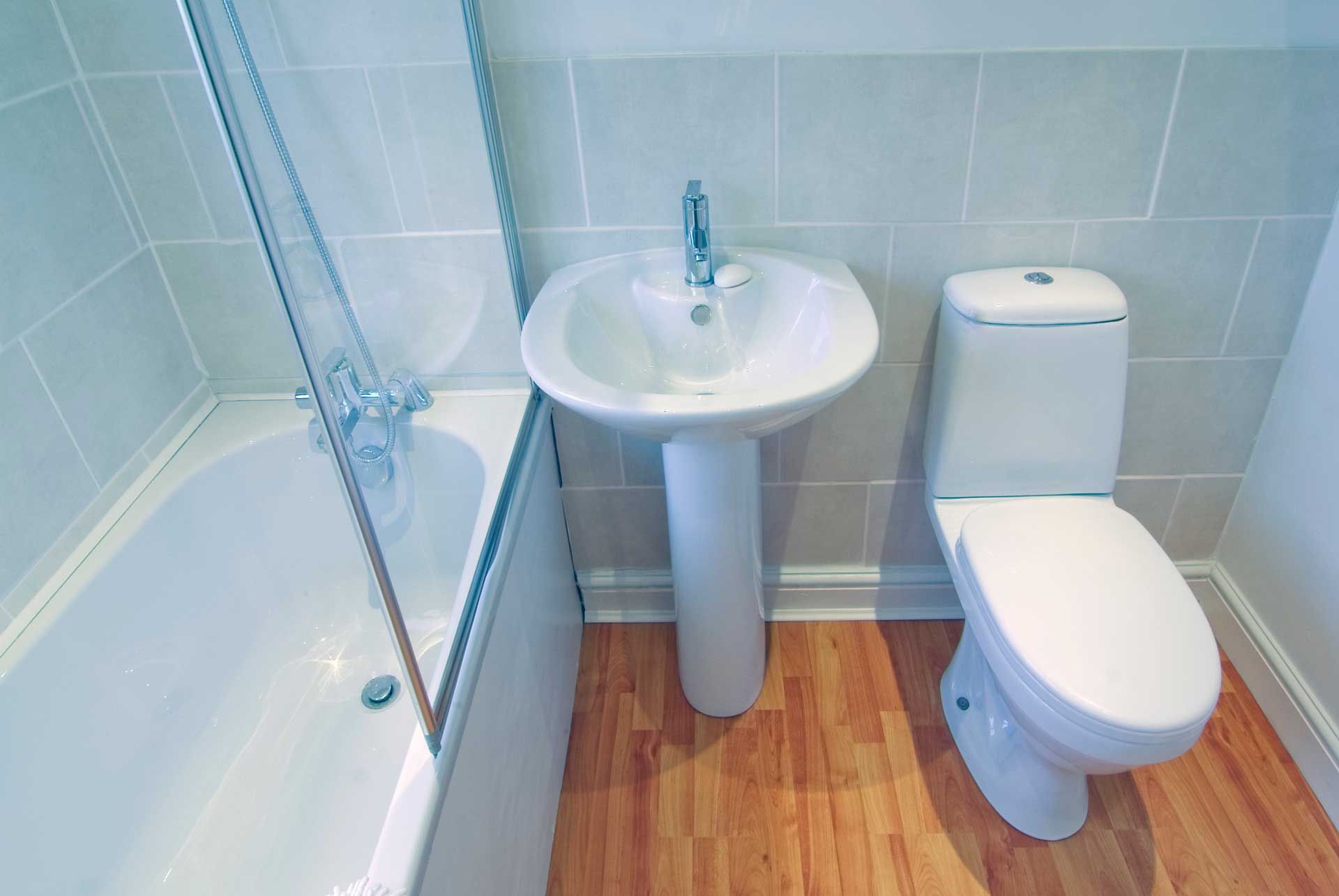 Bathroom with bathtub, pedestal sink, and toilet, with wooden floor and tiled walls.