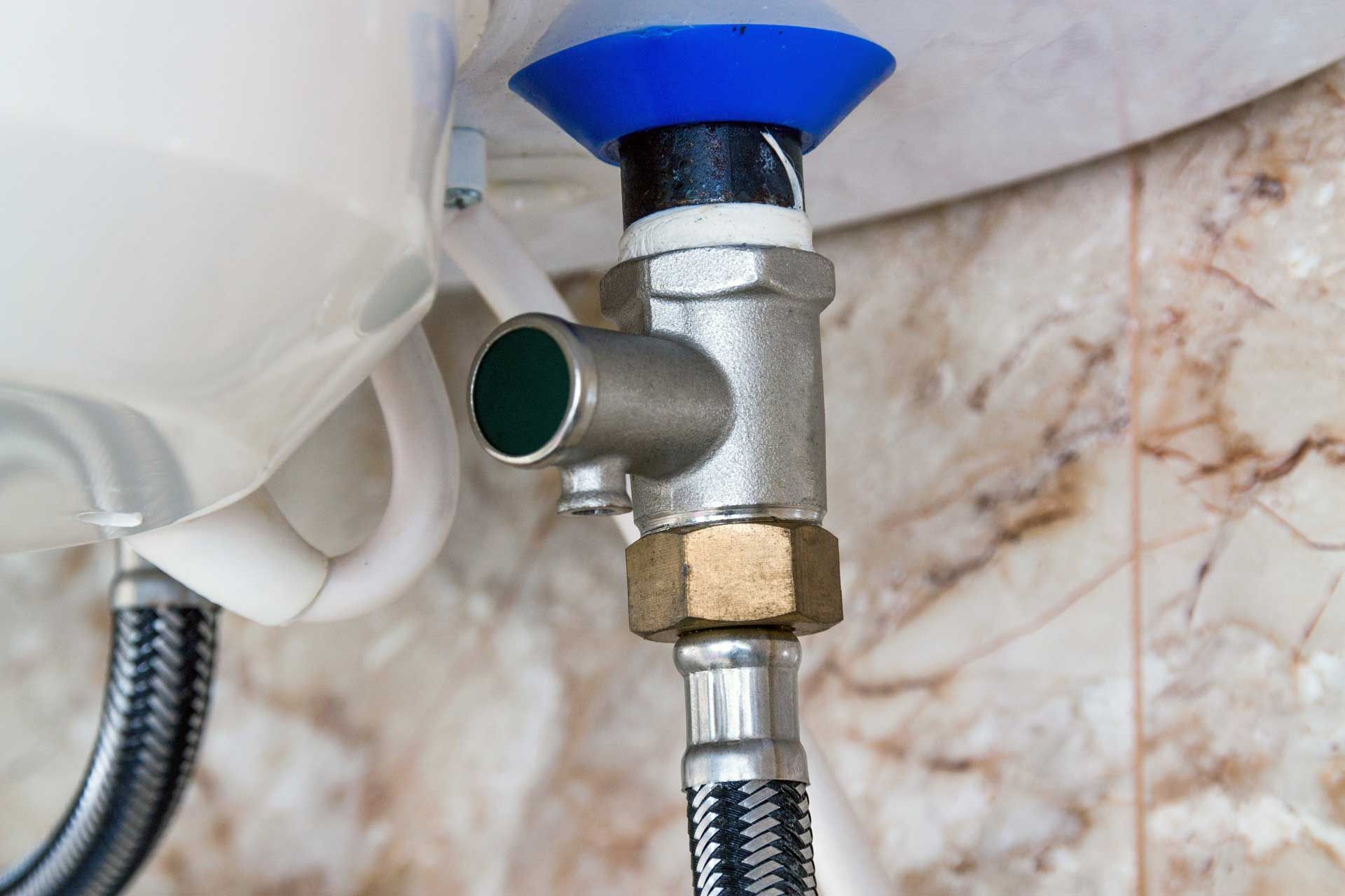 Close-up of a water heater relief valve and associated plumbing against a patterned wall.