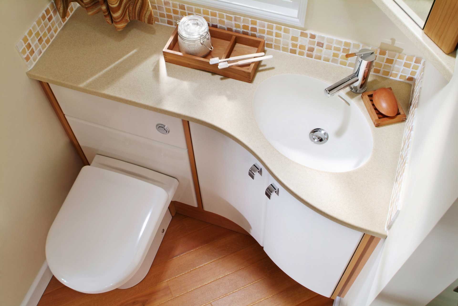 Bathroom in a camper with a toilet, sink, countertop, and wood flooring.
