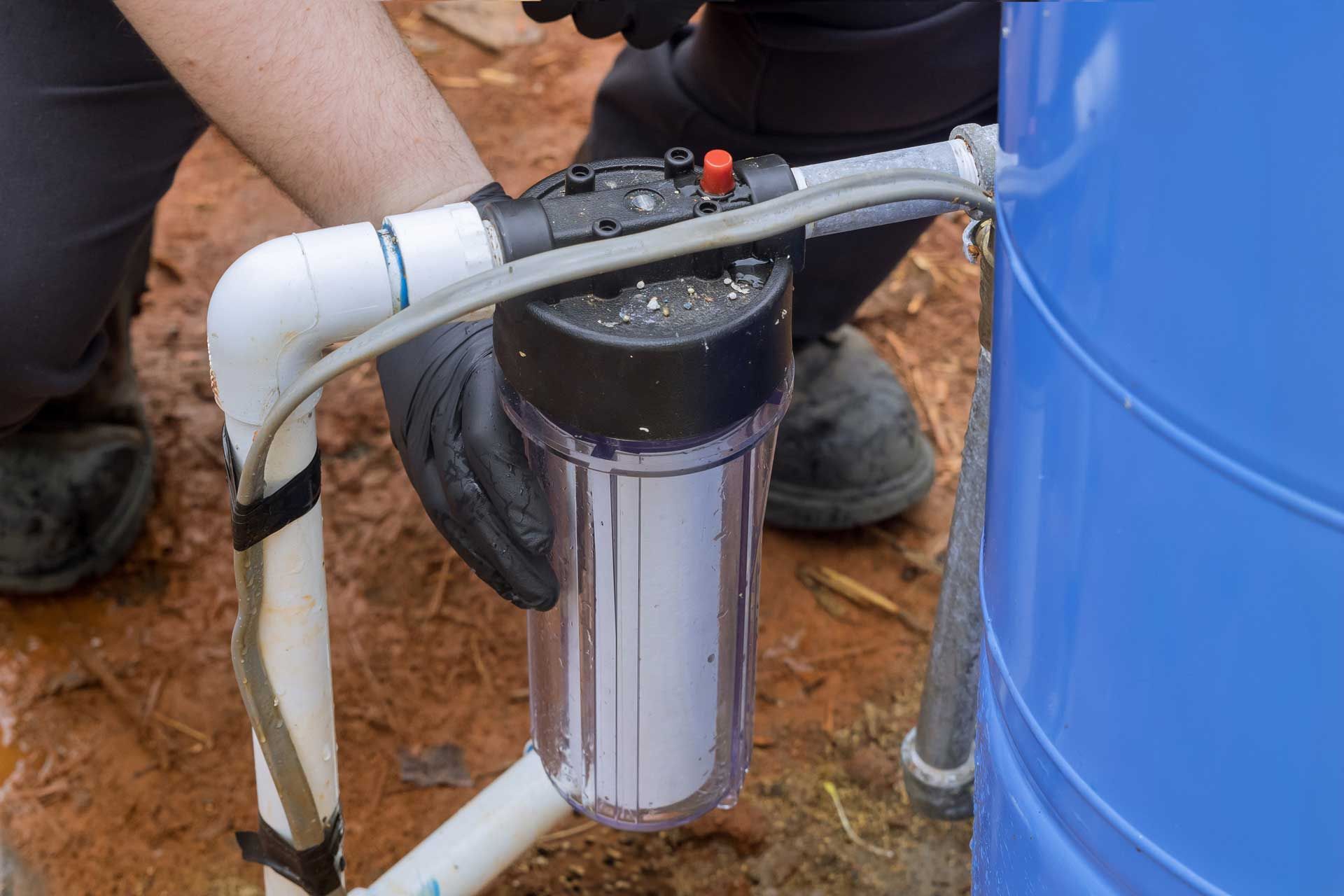 Person in gloves installing a water filter on a blue tank, outdoor setting.