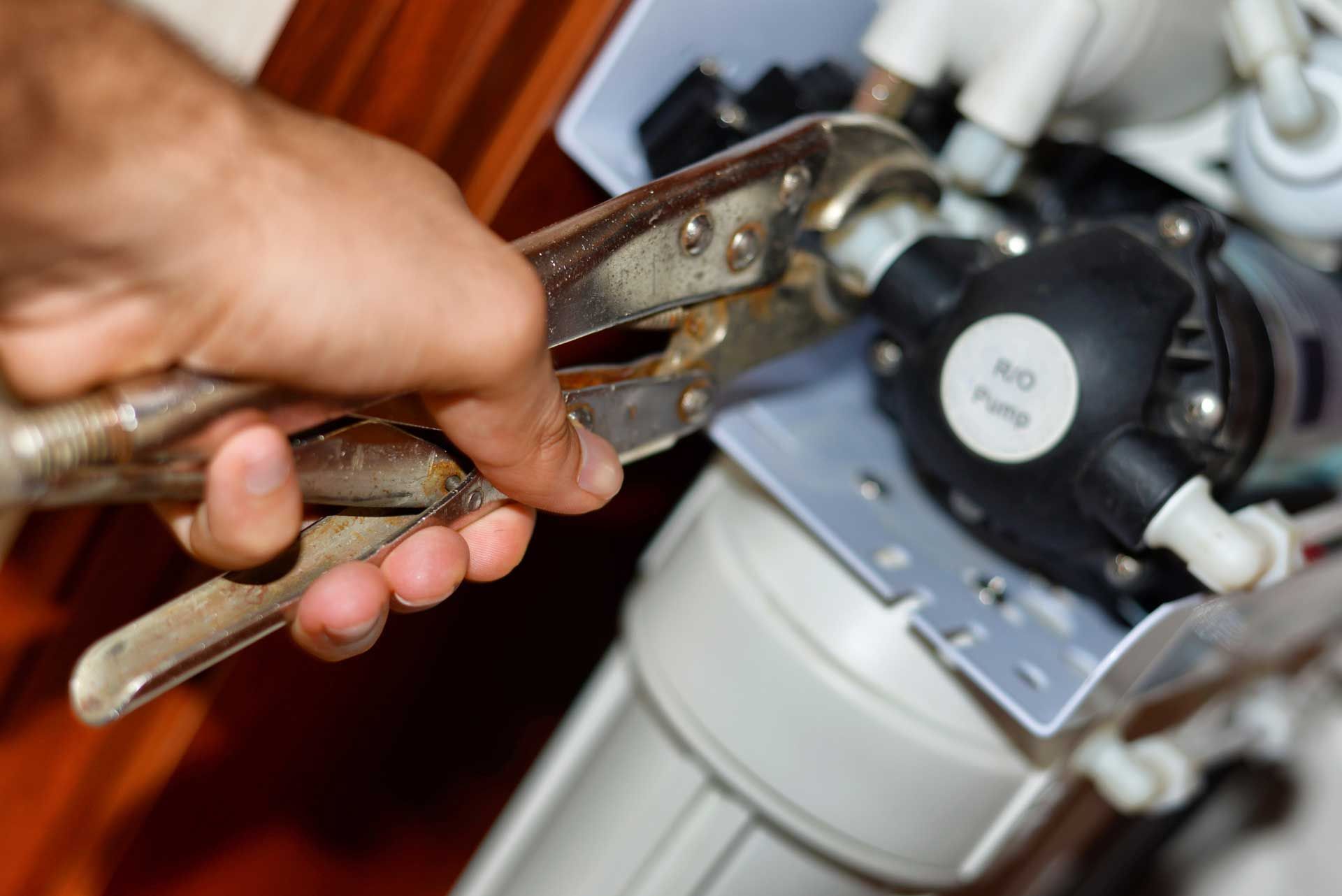 Person uses pliers to tighten a connection on a water filter system.