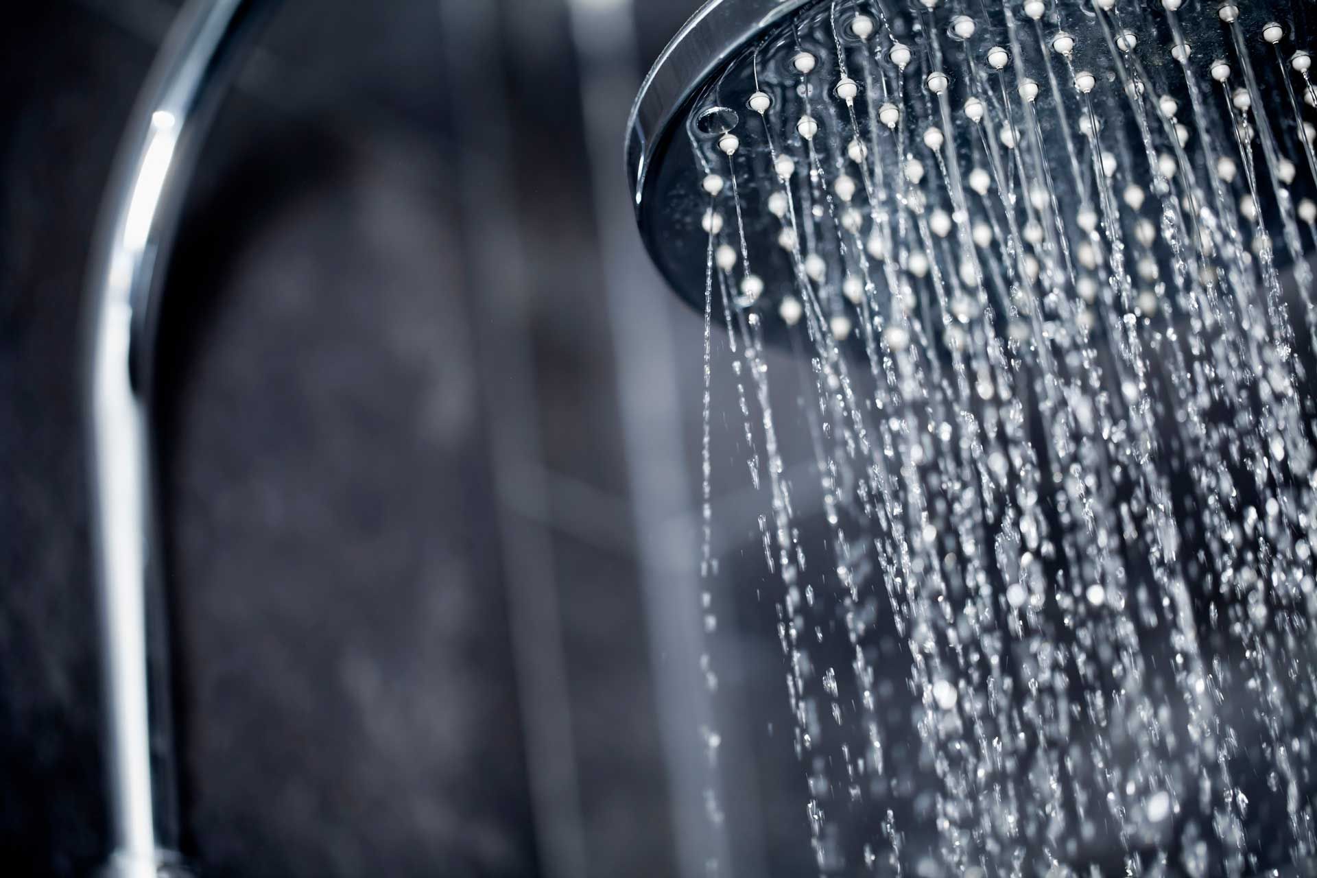 Showerhead releasing streams of water, close-up with a dark, blurred background.