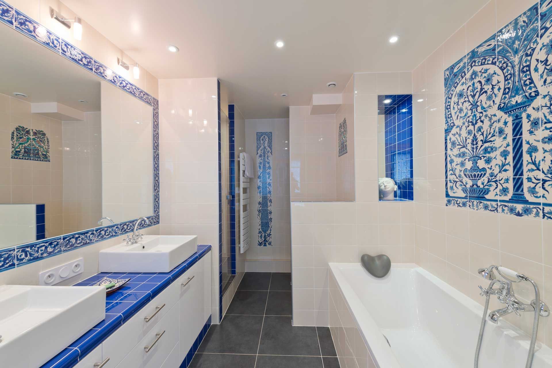 Blue and white Moroccan-style bathroom with rectangular sinks, bathtub, shower, and decorative tile.