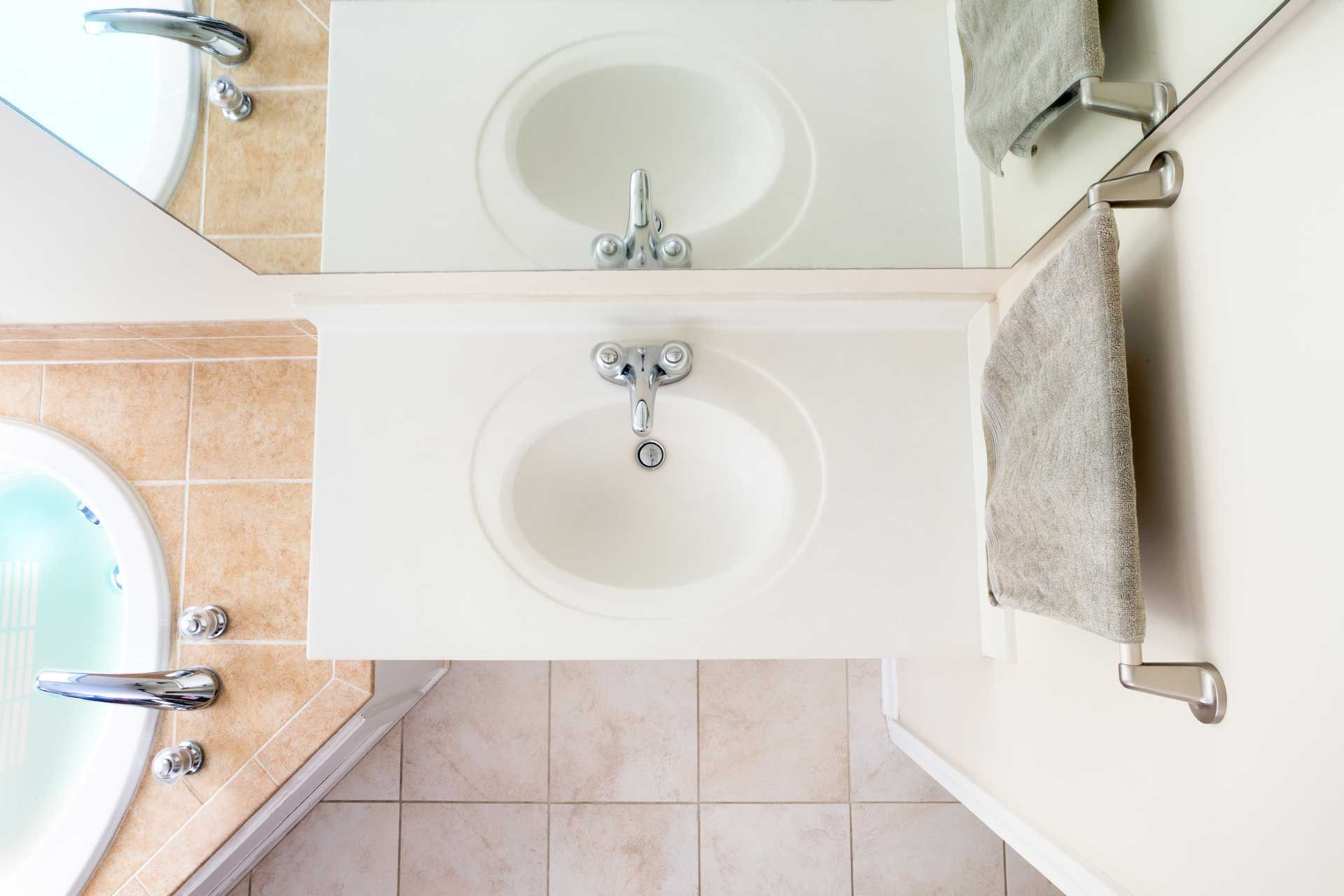 Bathroom with two sinks, a mirror, a towel rack, and a bathtub with beige tiled walls and floor.
