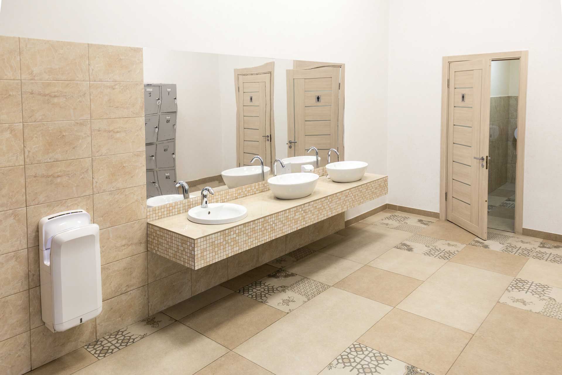 Public restroom with three sinks, two stalls, and tile flooring.