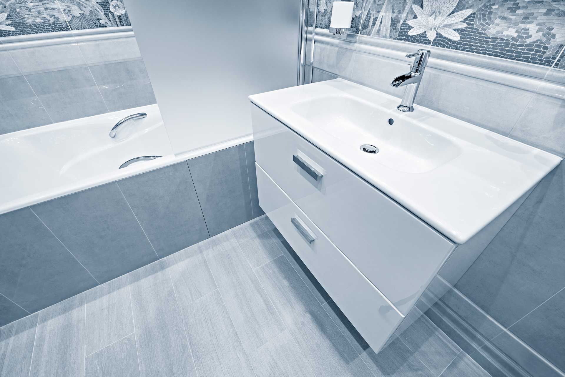 Bathroom with white vanity, sink, and tub. Gray tile walls and floor.