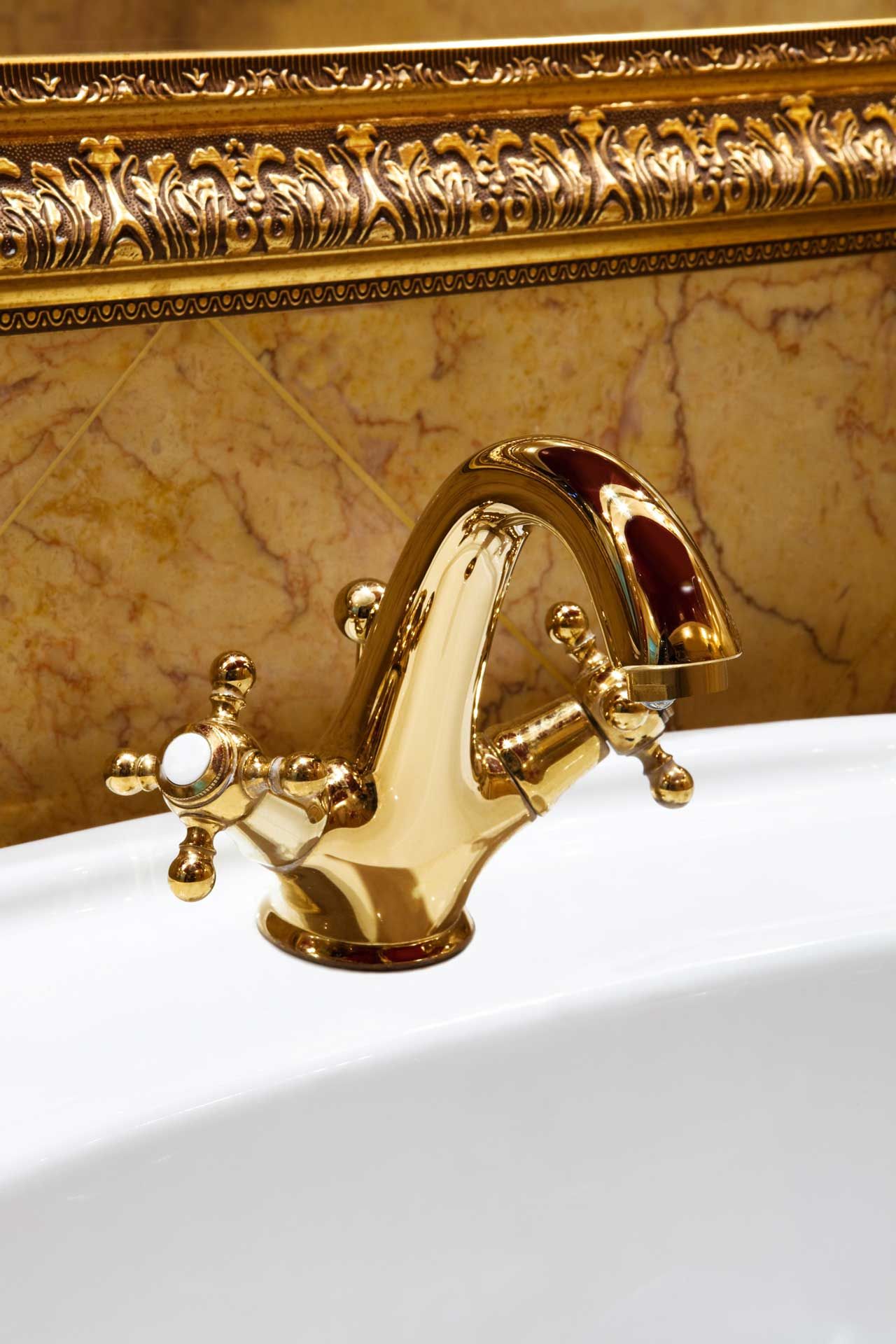 Gold faucet in a white sink, with decorative gold and marble background.